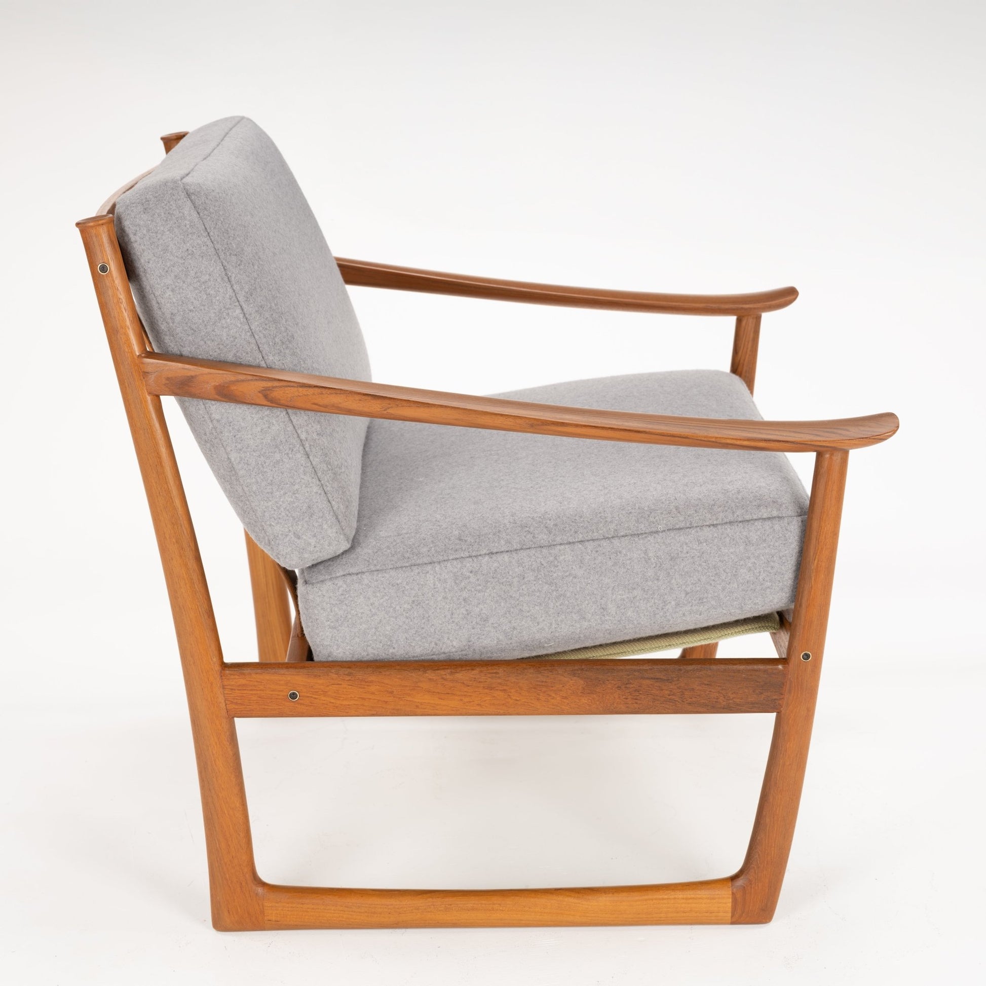Side profile of a mid-century style armchair with grey cushions and a warm wooden frame on a white background