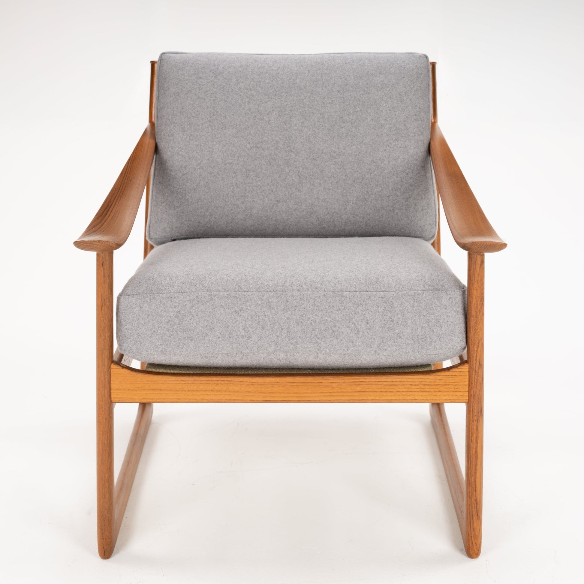 Straight-on view of a wooden armchair with light grey cushions and slim armrests on a white background