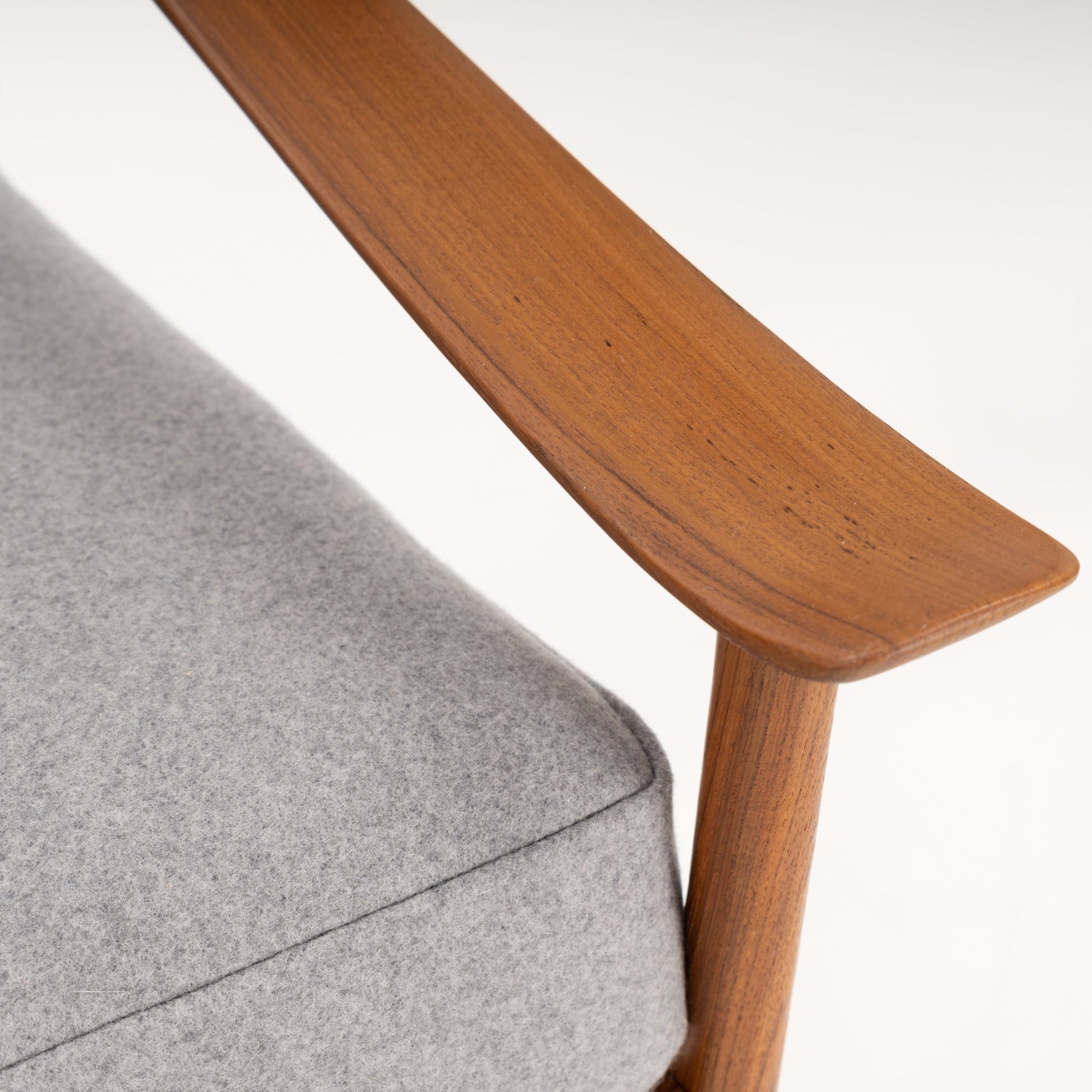 Close-up of a smooth wooden armrest and light grey upholstered cushion on a mid-century style chair against white background
