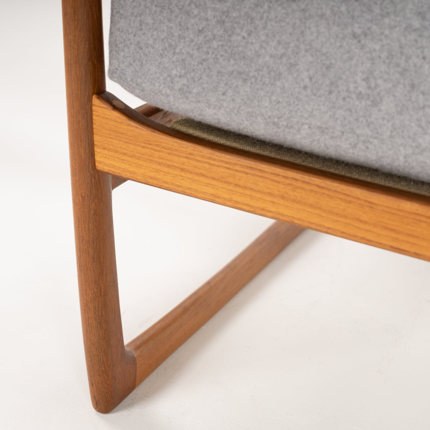 Close-up of smooth wooden chair leg and frame with light grey upholstered cushion against white background