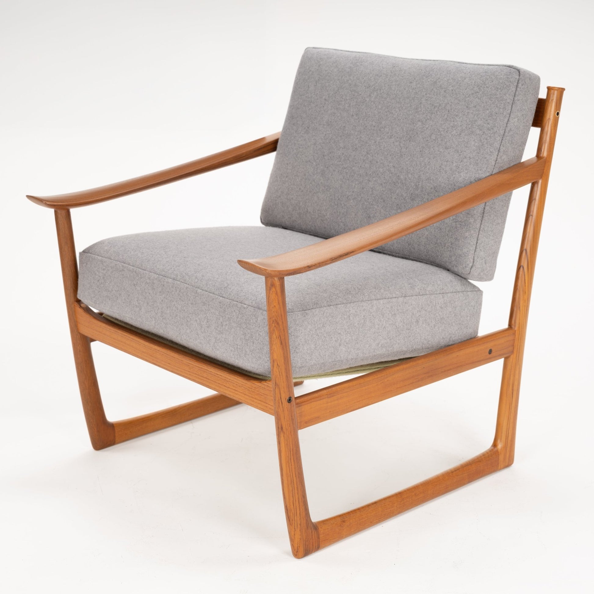 Angled view of a wooden framed armchair with smooth armrests and thick grey cushions on a white background