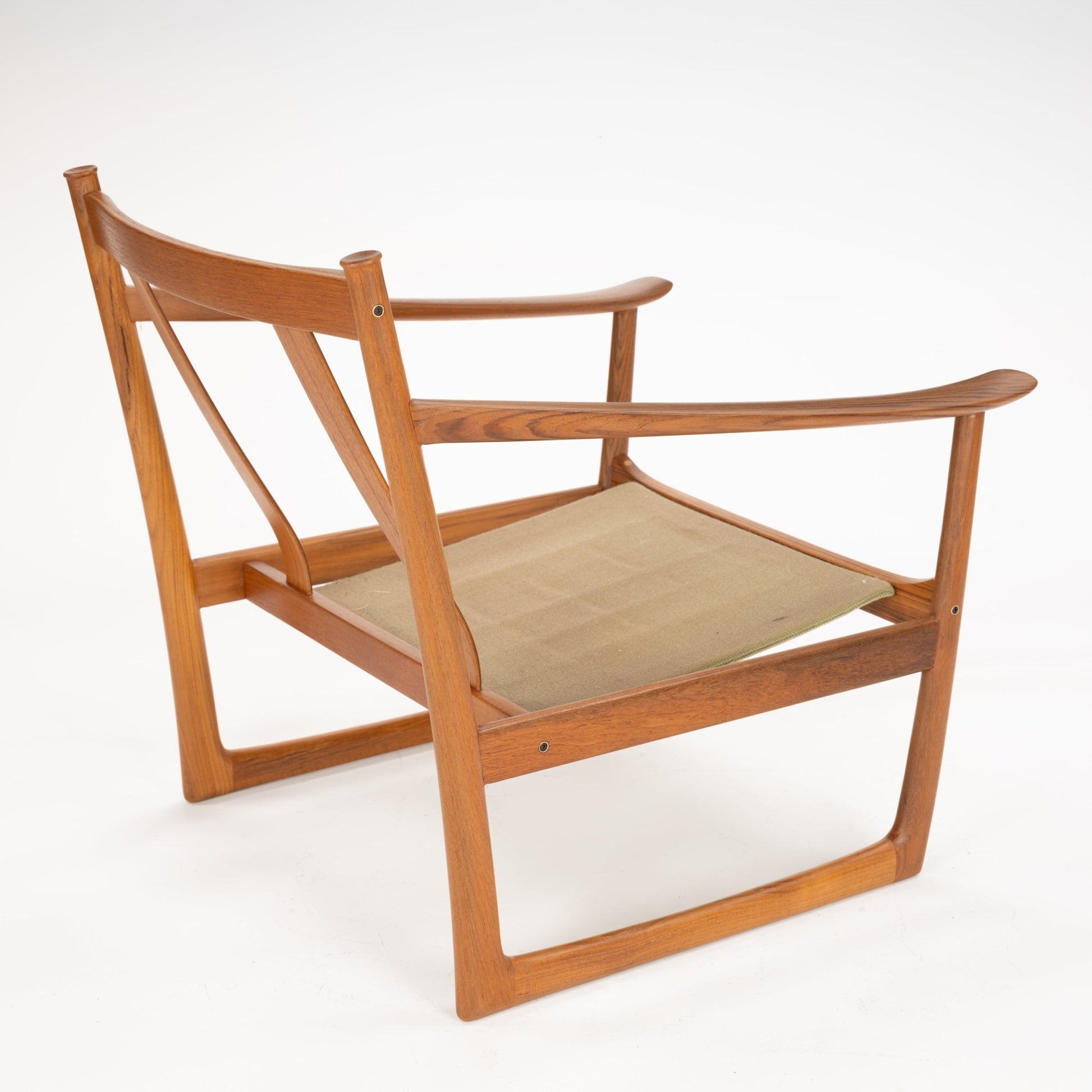 Angled side view of a wooden chair frame with curved armrests and a beige fabric sling seat on white background