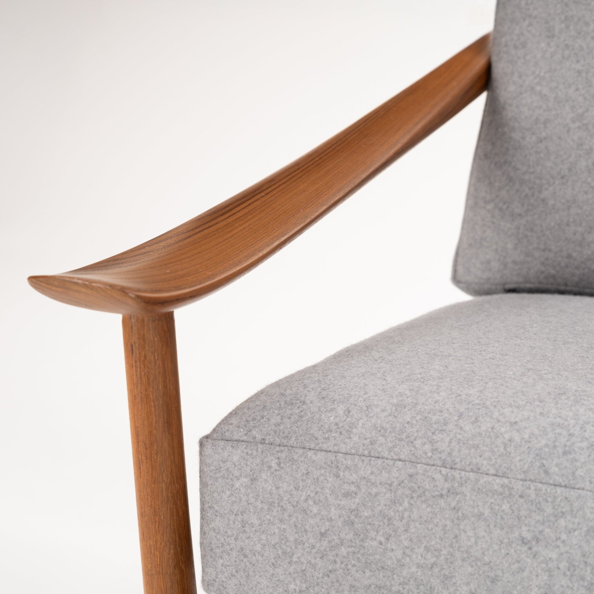 Close-up of finely crafted wooden armrest and leg with soft light grey fabric cushion on a modern armchair