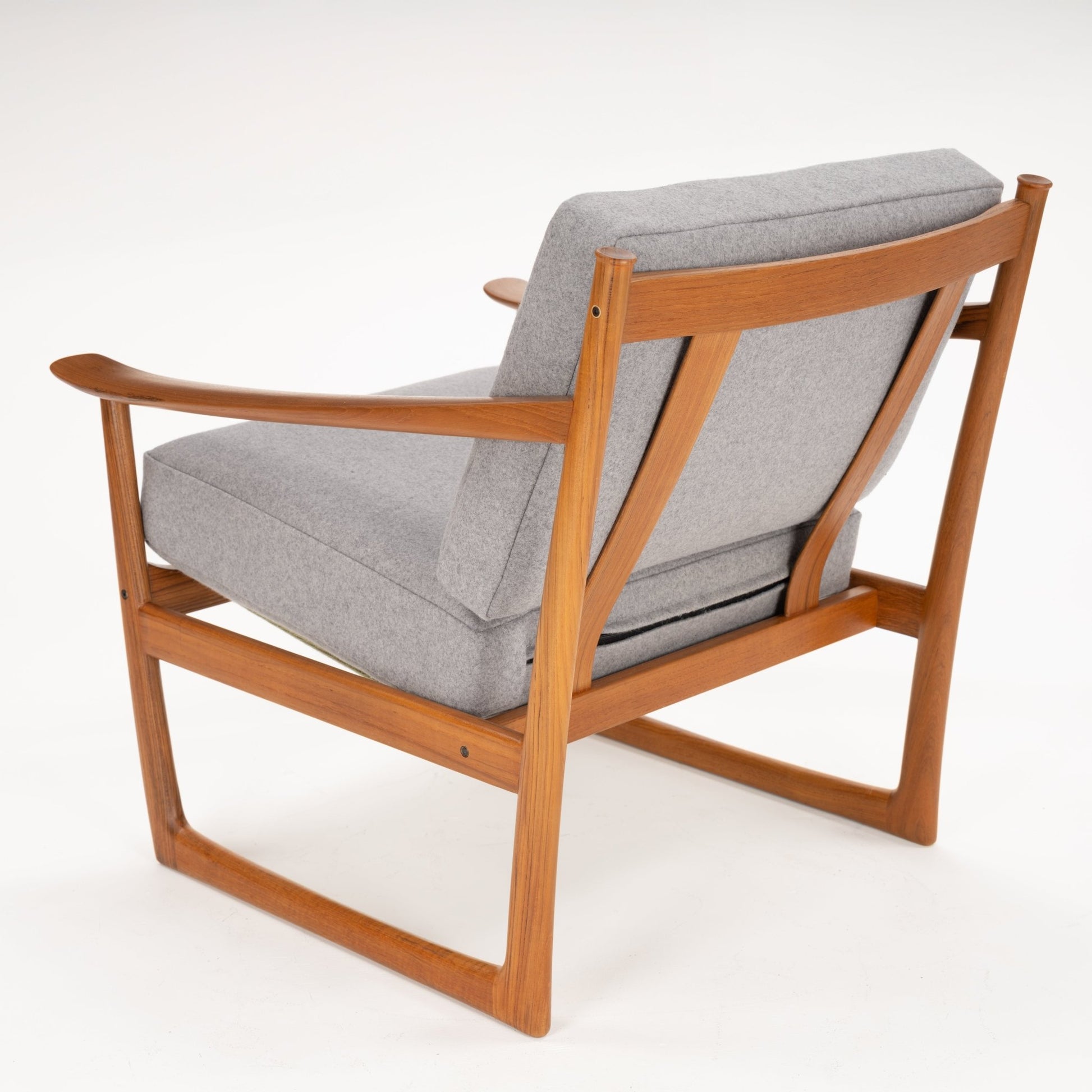 Rear angled view of a wooden frame armchair with a light grey cushioned seat and backrest on white background