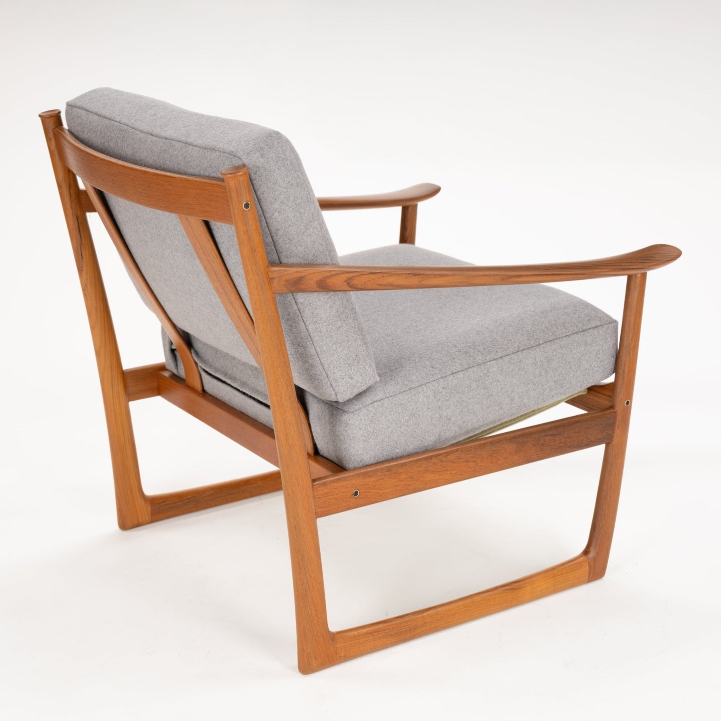 Back angled view of a wooden frame armchair with curved armrests and thick light grey cushions on white background