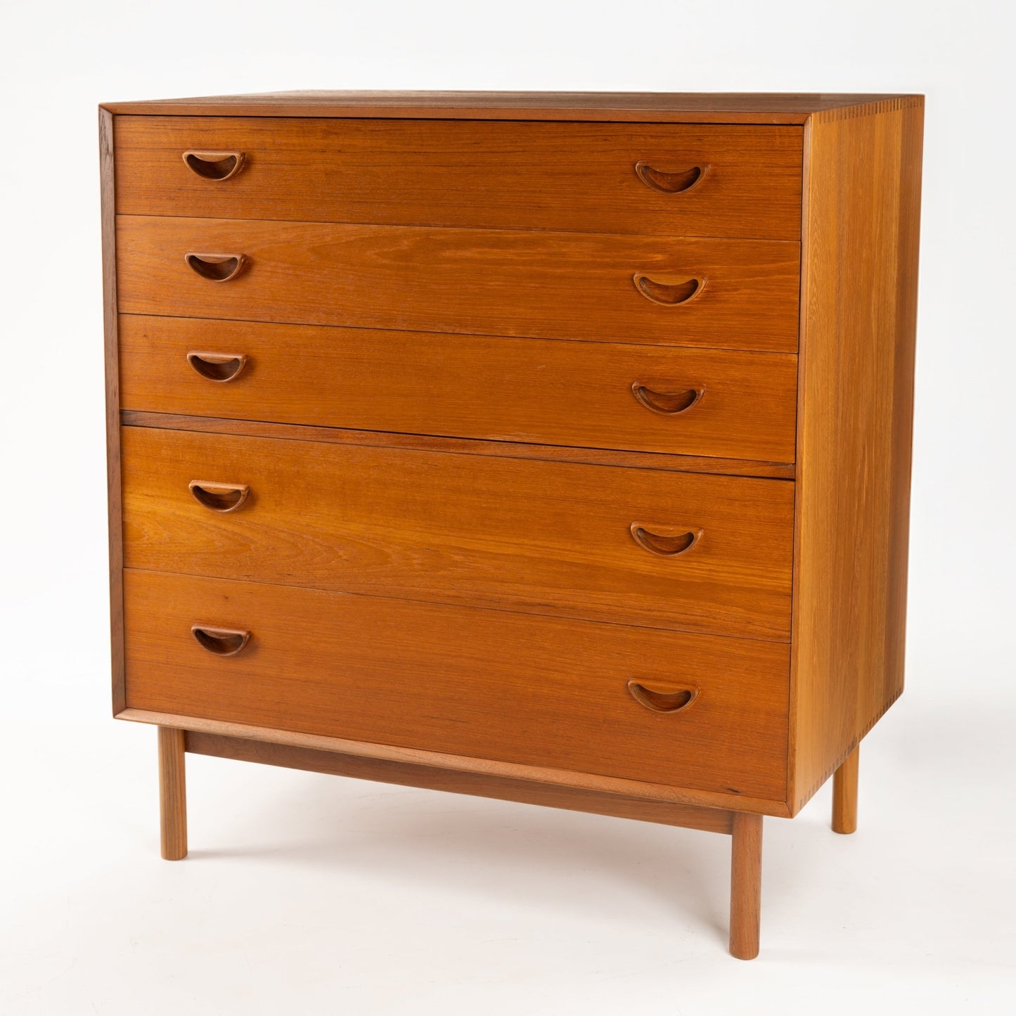 Peter Hvidt & Orla Nielsen Teak Chest of Drawers with warm teak finish, featuring five drawers with sculpted recessed handles and standing on slender round legs in vintage mid century modern style.