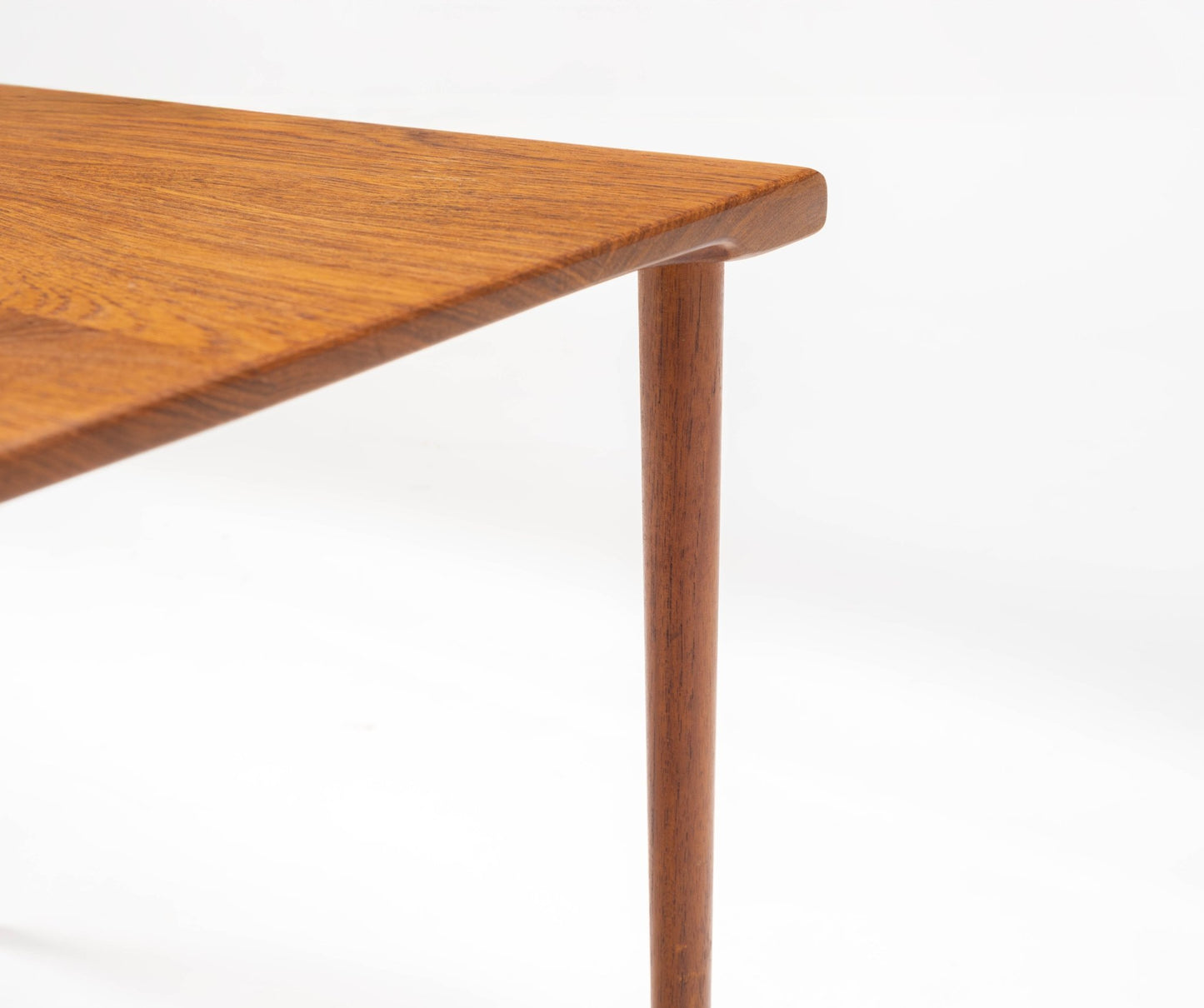 Close-up of Peter Hvidt mid-century modern teak side table corner with slender tapered dowel leg on white background