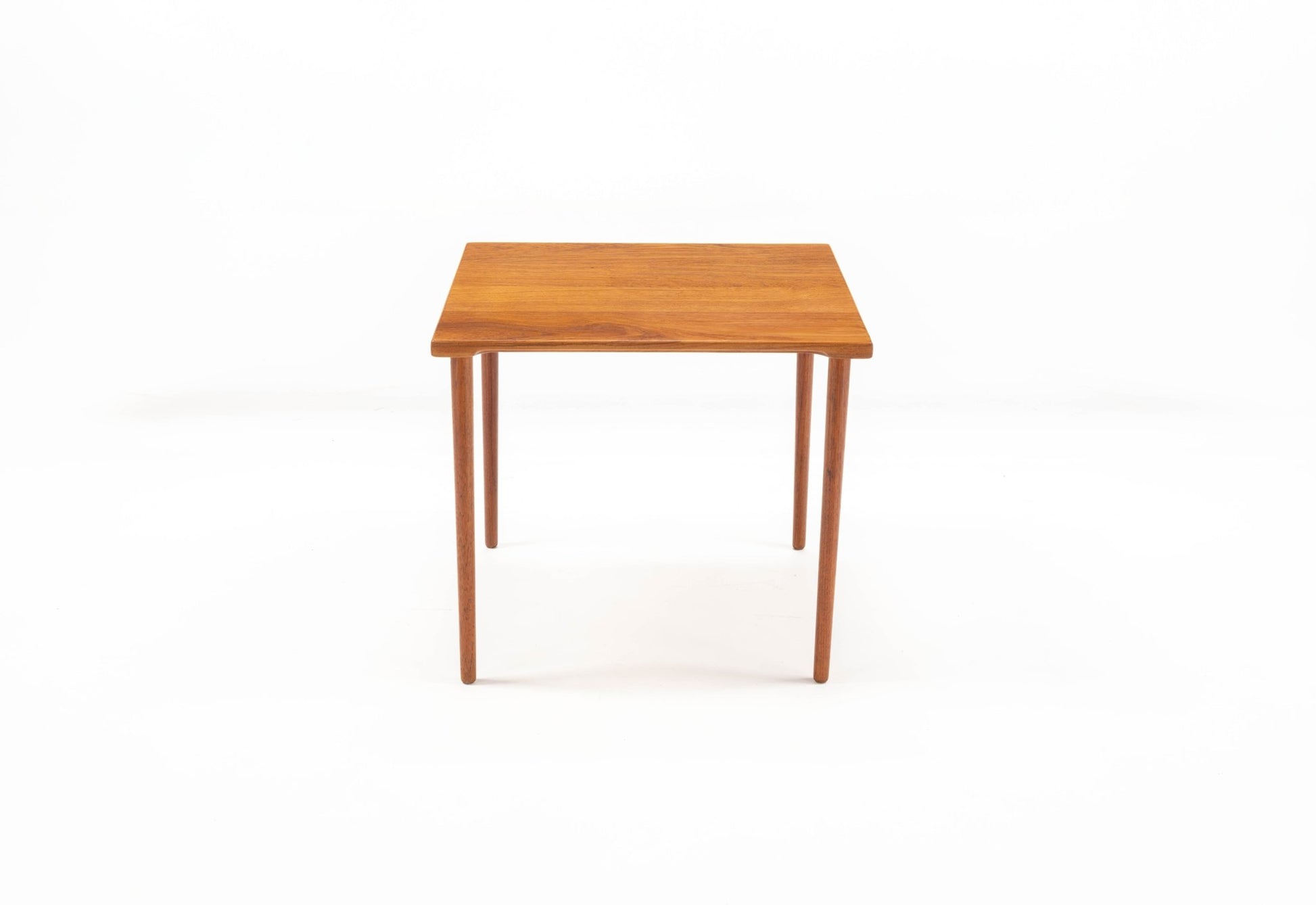 Mid-century modern Peter Hvidt teak side table with square top and slender dowel legs on white background.