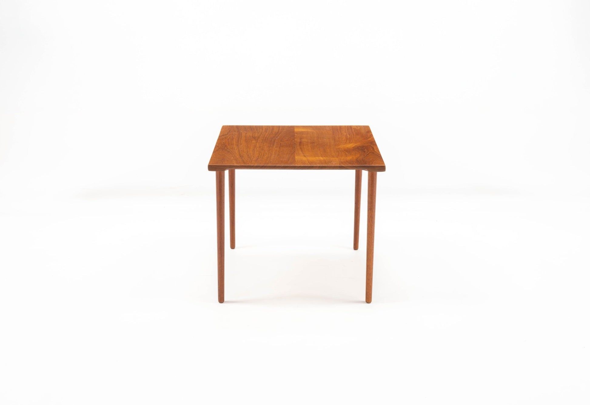 Mid-century modern Peter Hvidt teak side table with slender dowel legs and single slab wood top on white background
