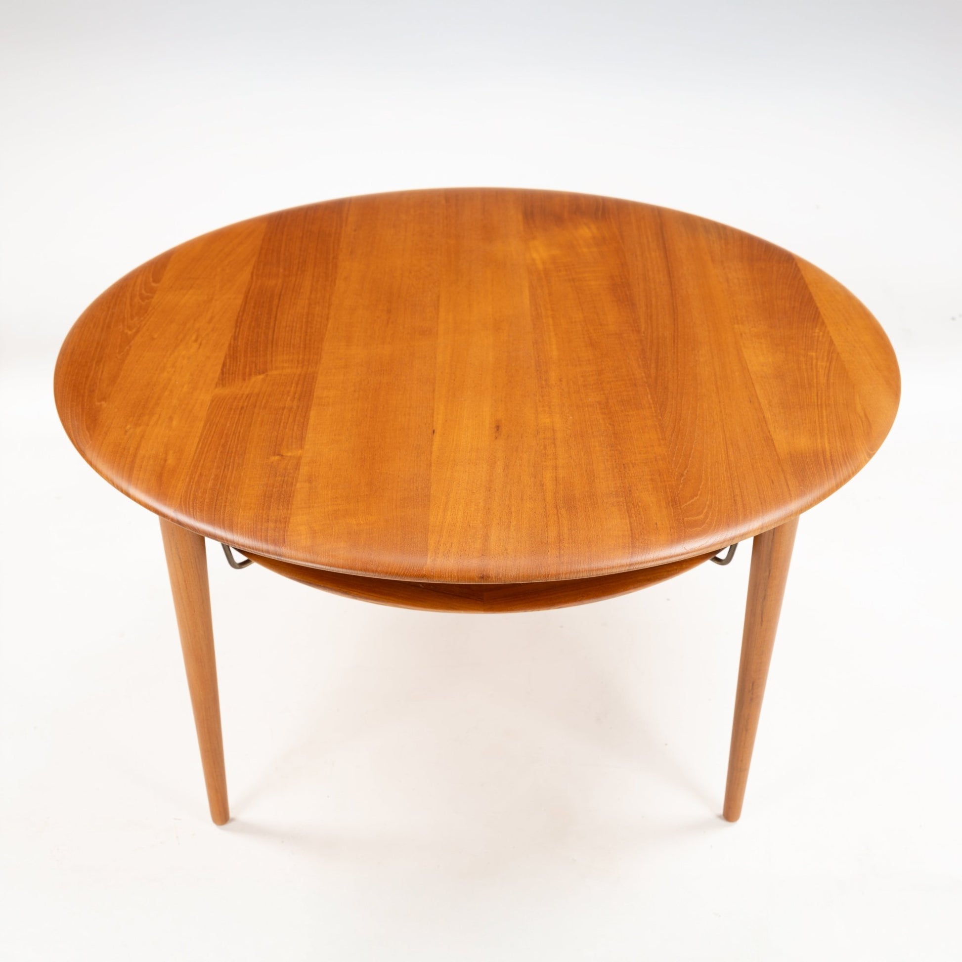 Peter Hvidt Teak Coffee Table Model FD-515 featuring a smooth round teak surface with a warm honey tone and tapered legs supporting a woven lower shelf in mid century modern style.