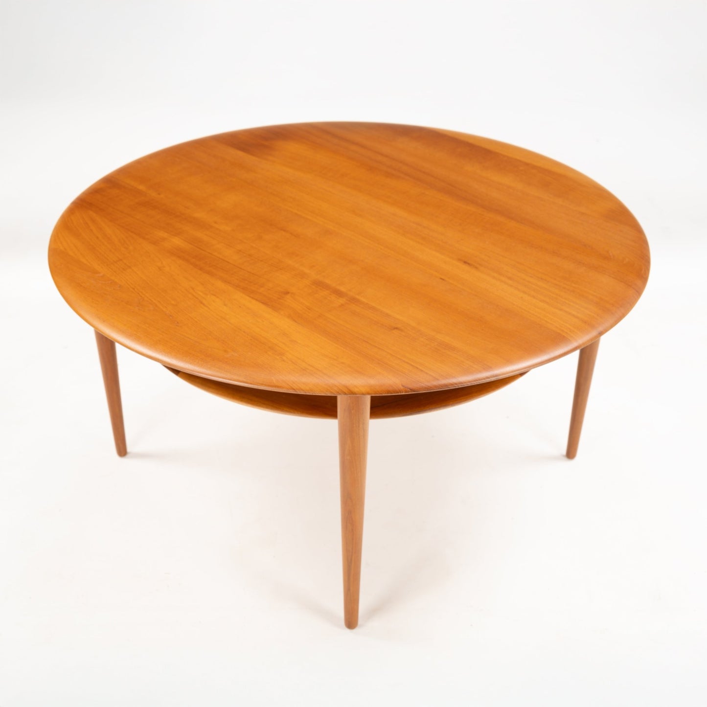 Peter Hvidt Teak Coffee Table Model FD-515 with a smooth round teak top and tapered legs featuring a subtle lower circular shelf in classic mid century modern furniture style.