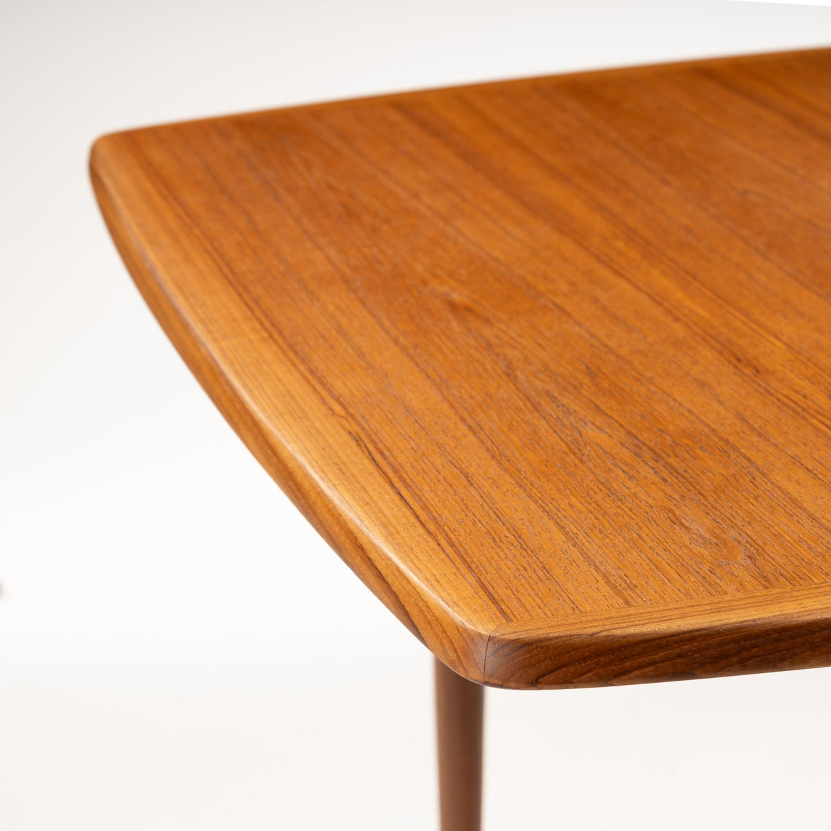 Rastad & Relling Extension Dining Table close-up highlighting rich teak grain a rounded tabletop edge and tapered leg in mid century modern furniture style