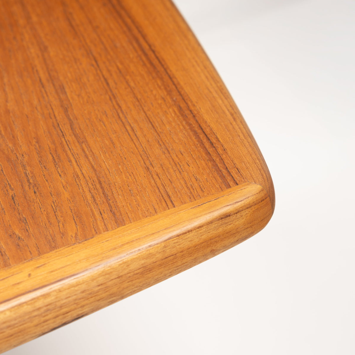 Rastad & Relling Extension Dining Table close detail showing warm teak grain and a softly rounded tabletop edge in mid century modern furniture style
