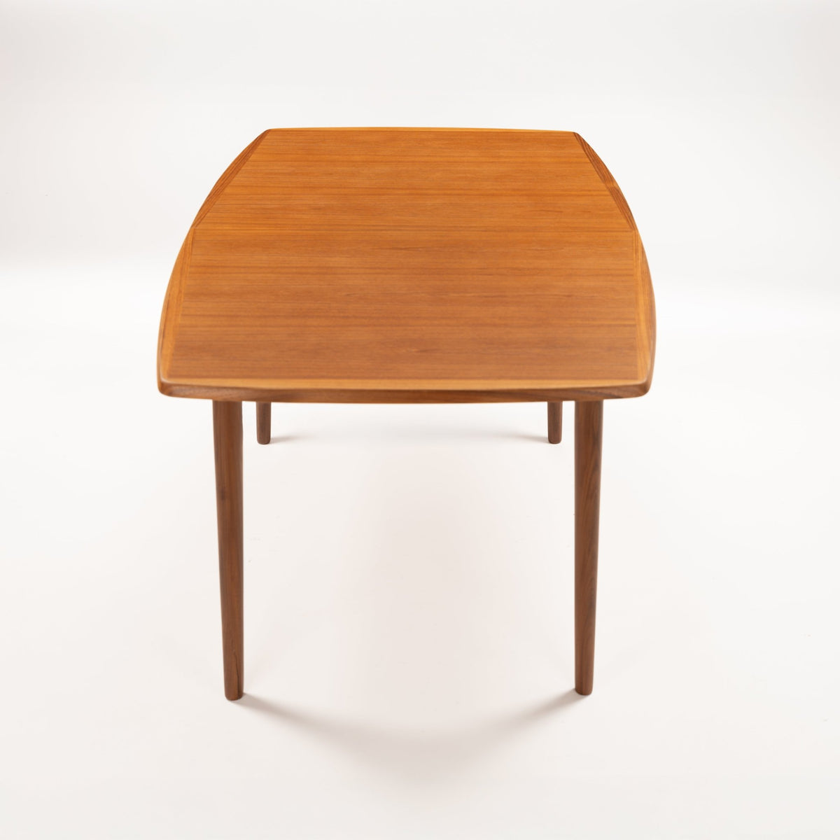 Rastad & Relling Extension Dining Table showing a closed warm teak top with curved corners and slender tapered legs in vintage Danish furniture style