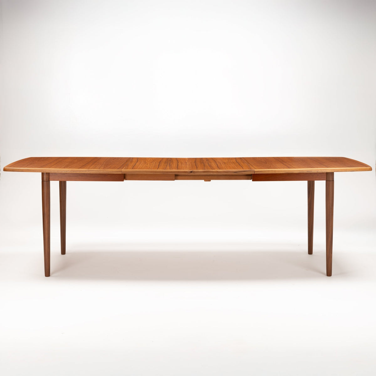 Rastad & Relling Extension Dining Table in polished teak with a long rounded top and tapered legs showcasing vintage danish furniture design