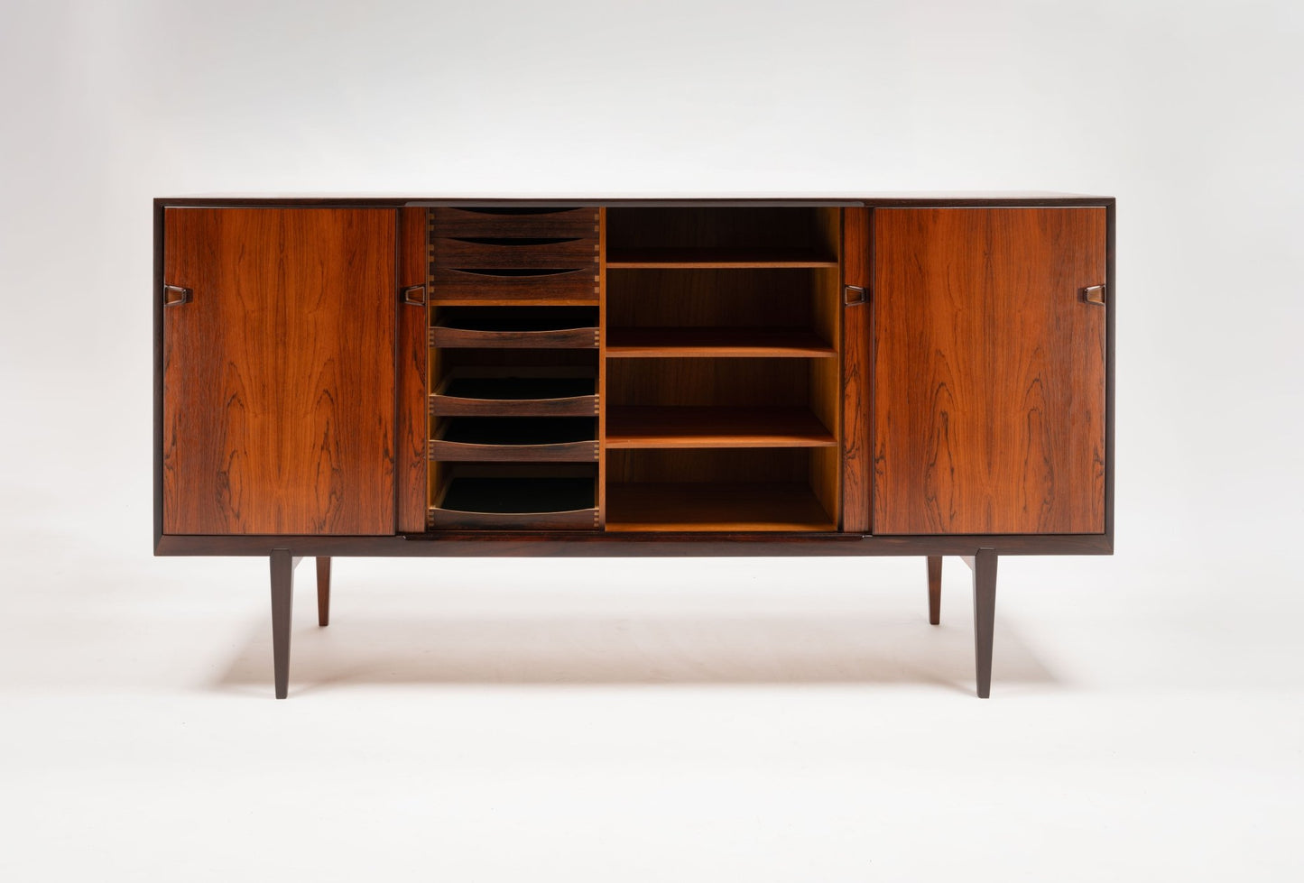 Mid-century modern rosewood credenza with sculpted handles, multiple compartments, and tapered legs on white background.
