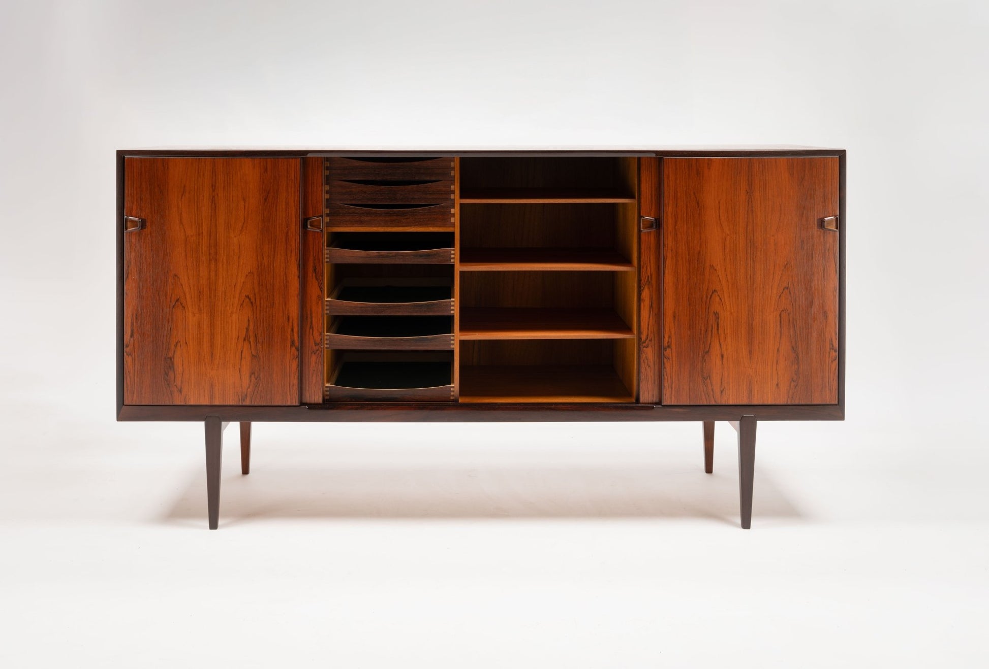 Mid-century modern rosewood credenza with sculpted handles, multiple compartments, and tapered legs on white background.