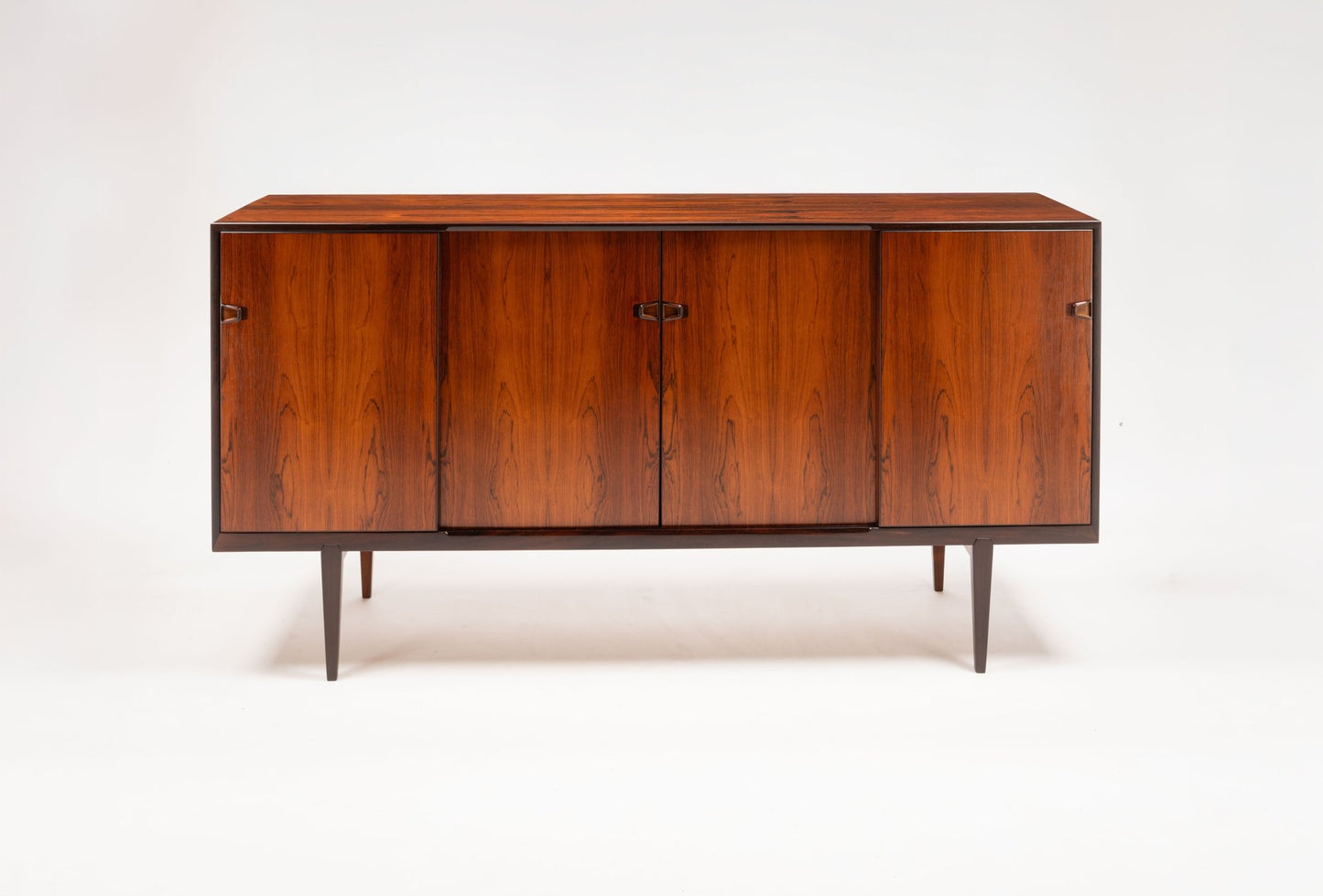 Mid-century modern rosewood credenza with sculpted handles, tapered legs, and rich wood grain on white background