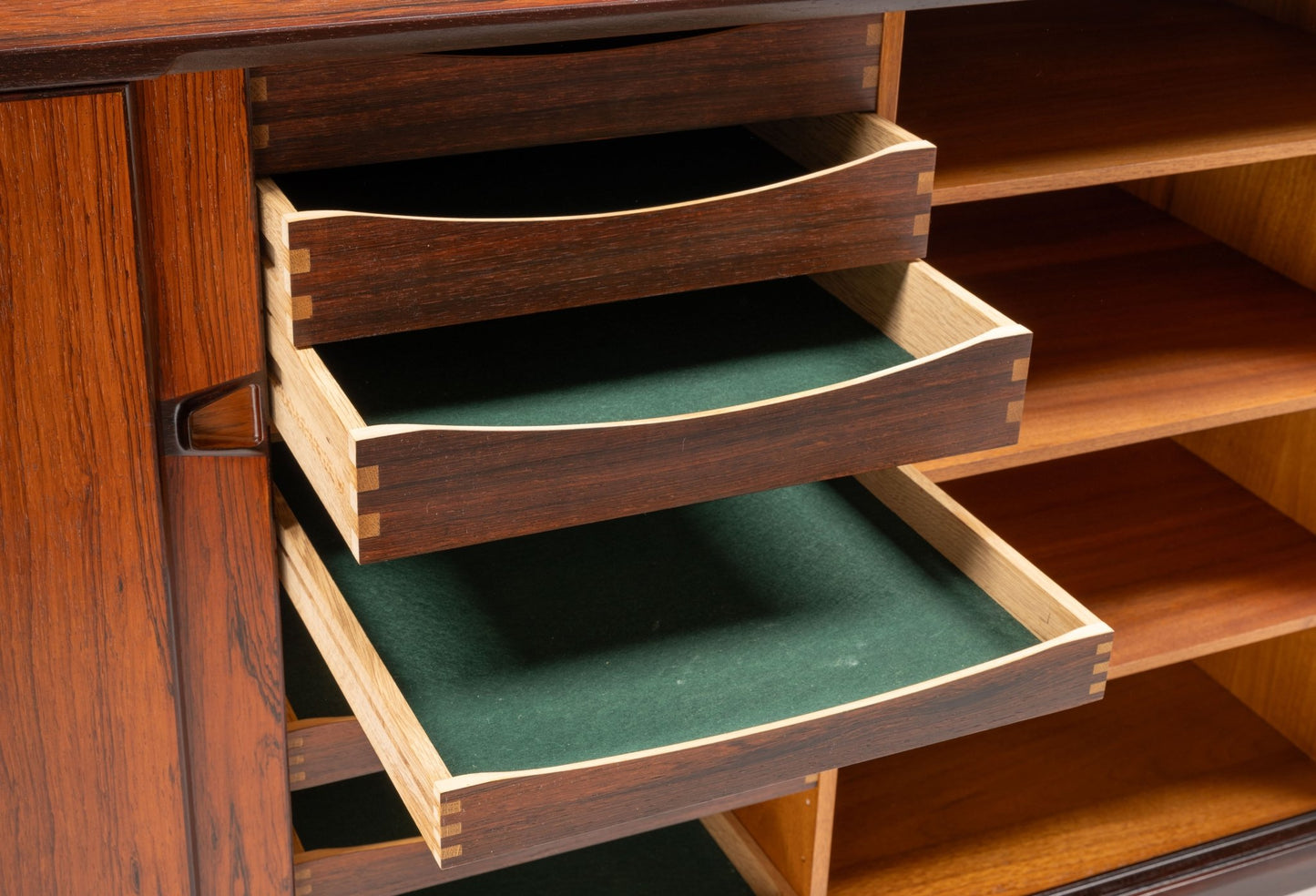 Close-up of mid-century modern rosewood credenza drawers with green felt lining and dovetail joints open on sideboard.