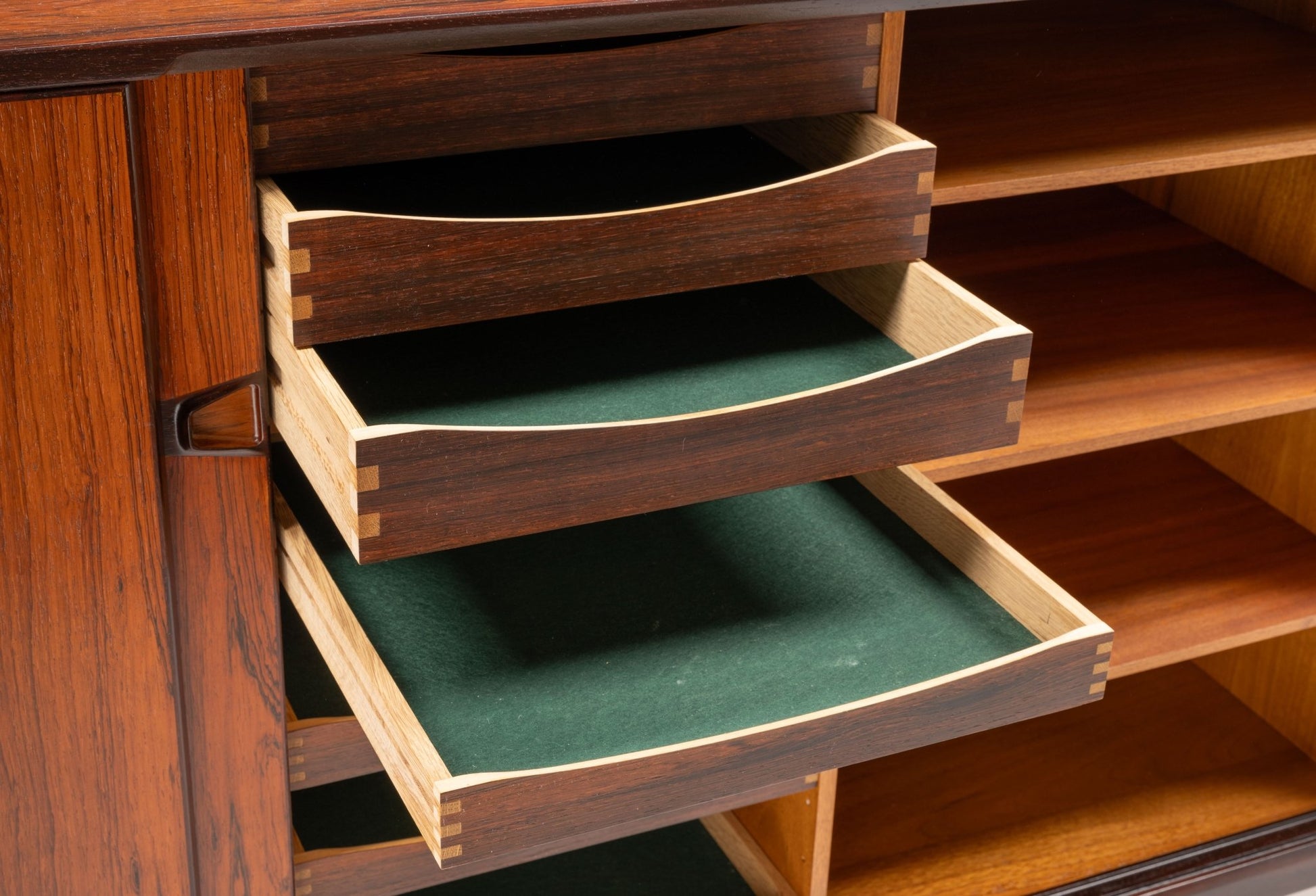 Close-up of mid-century modern rosewood credenza drawers with green felt lining and dovetail joints open on sideboard.