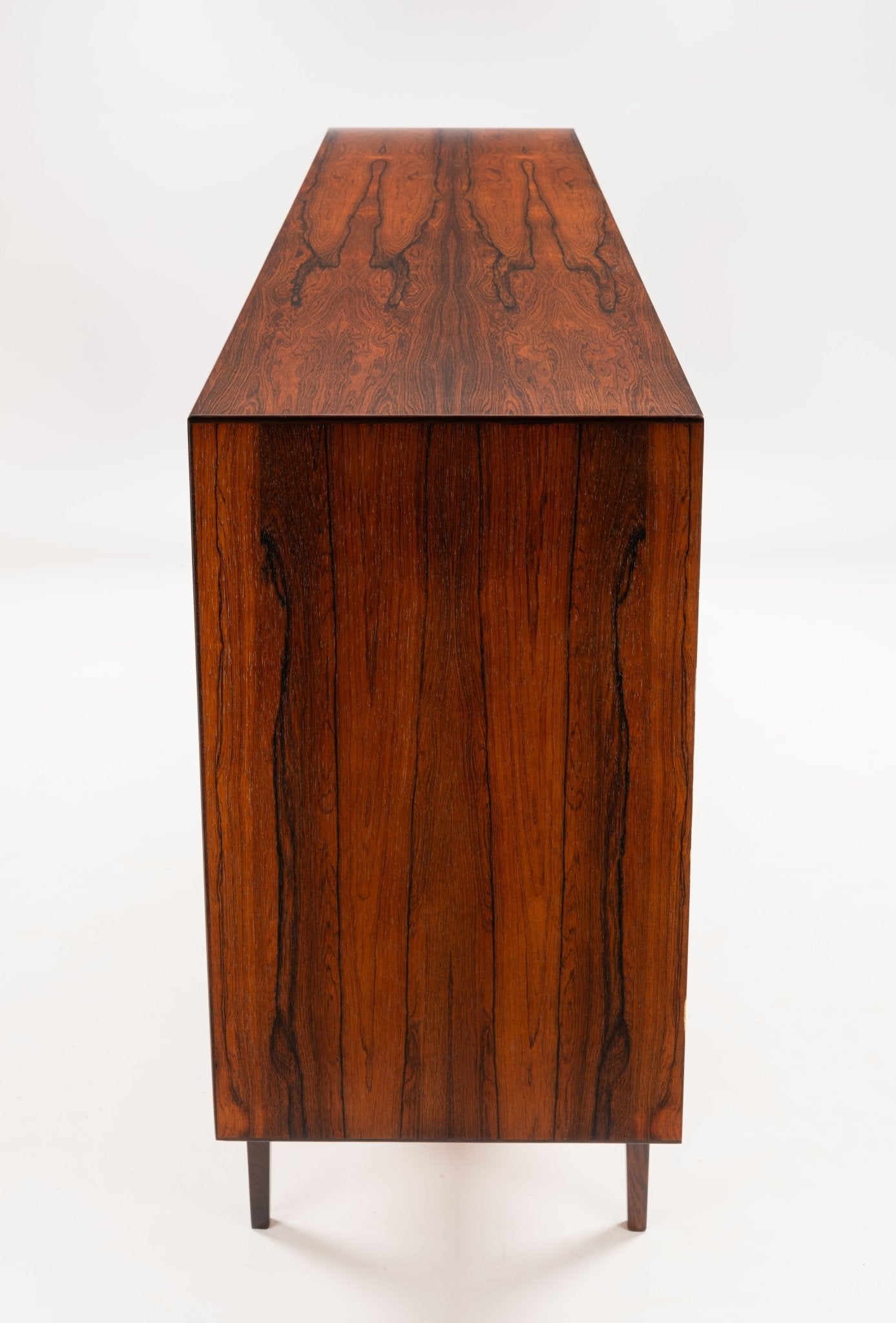 Side view of mid-century modern rosewood credenza with rich grain pattern and tapered legs on white background