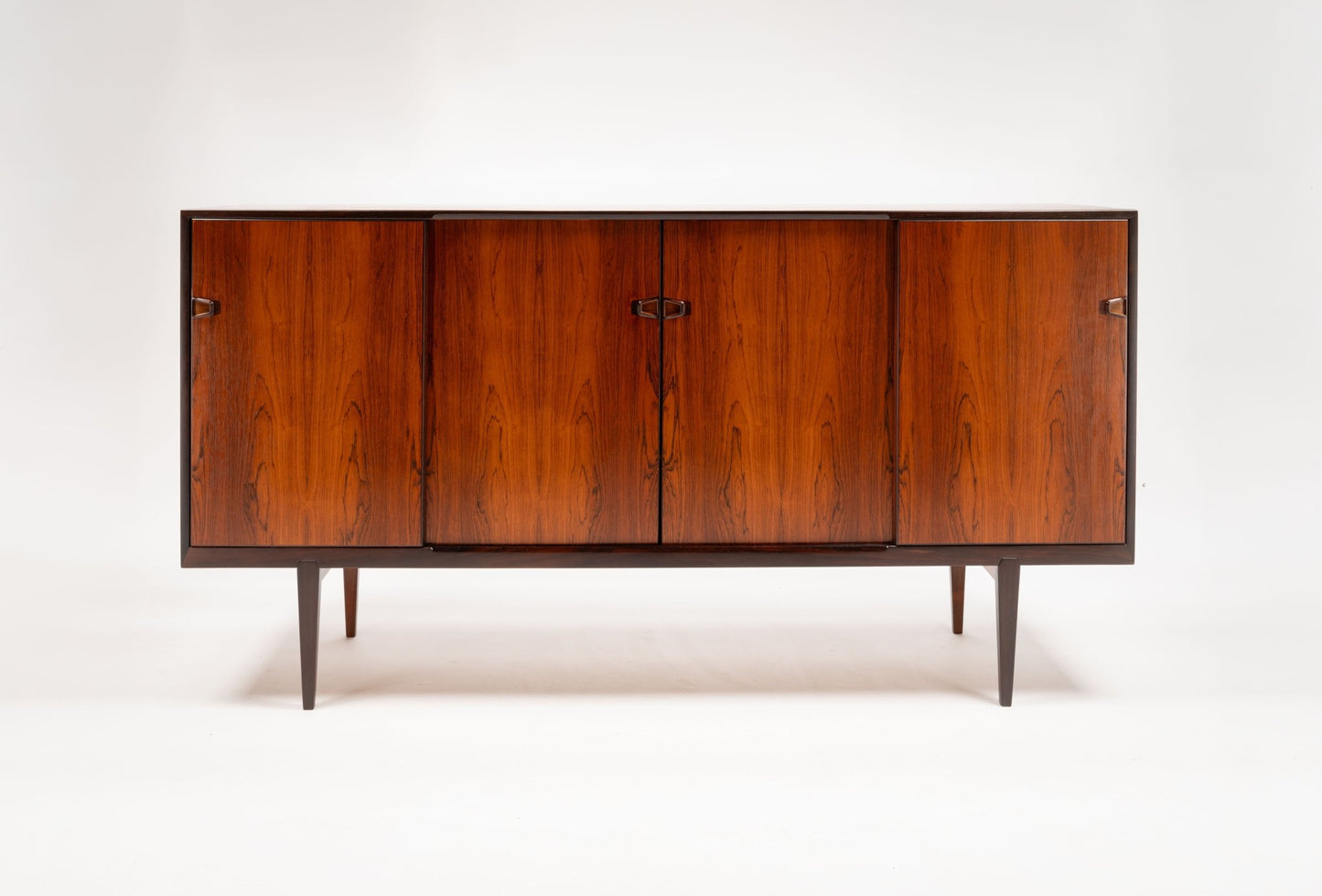 Mid-century rosewood credenza with sculpted handles and tapered legs, showcasing rich wood grain and minimalist design.