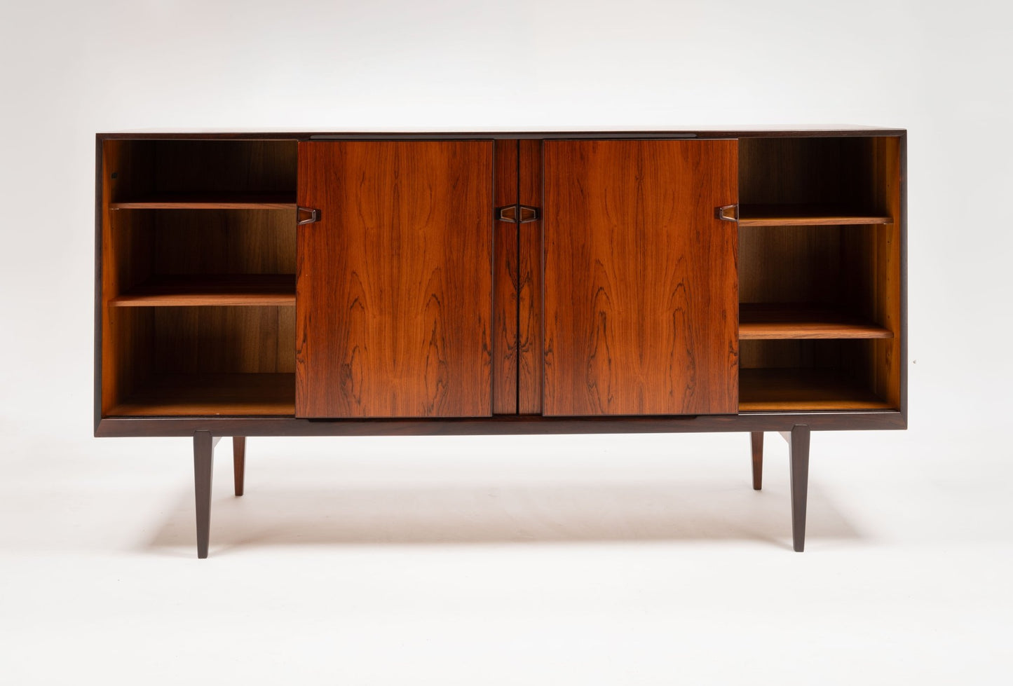 Mid-century modern rosewood credenza with sculpted handles, tapered legs, and open shelving on either side.