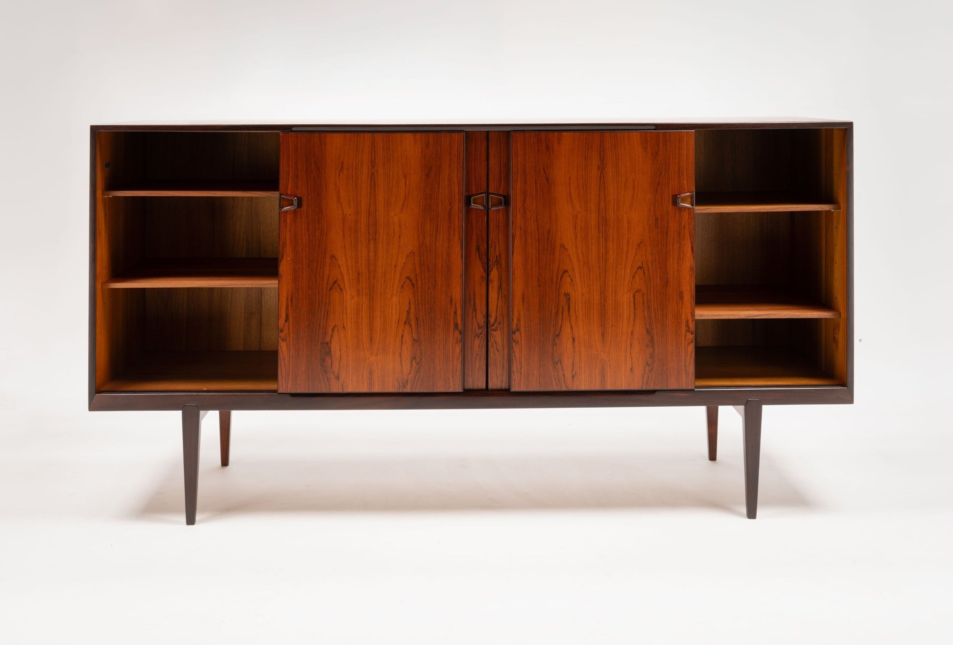 Mid-century modern rosewood credenza with sculpted handles, tapered legs, and open shelving on either side.