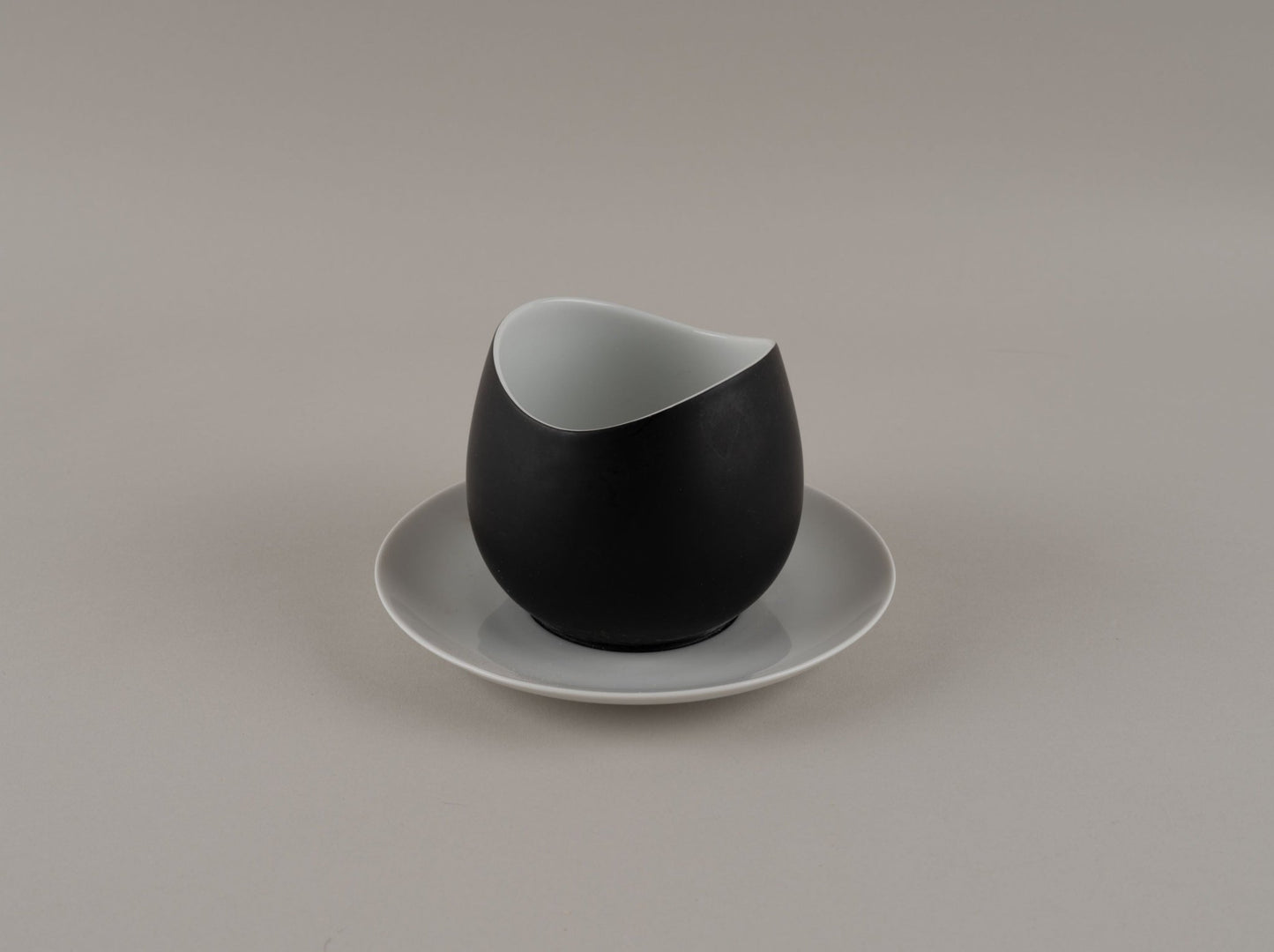 Rosenthal "Charcoal" eggshell black cream pitcher with smooth modern design on a white saucer by Raymond Loewy