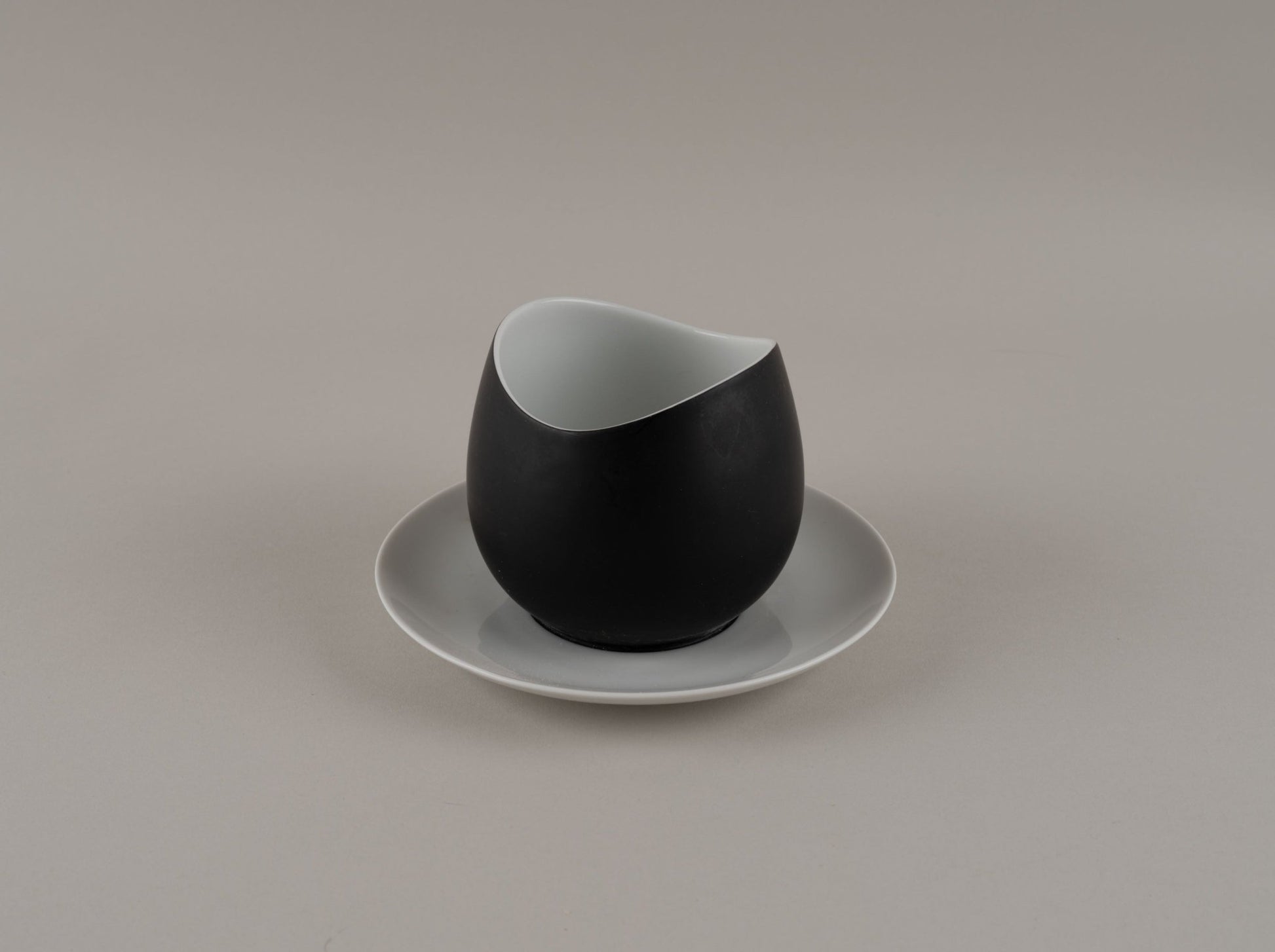 Rosenthal "Charcoal" eggshell black cream pitcher with smooth modern design on a white saucer by Raymond Loewy