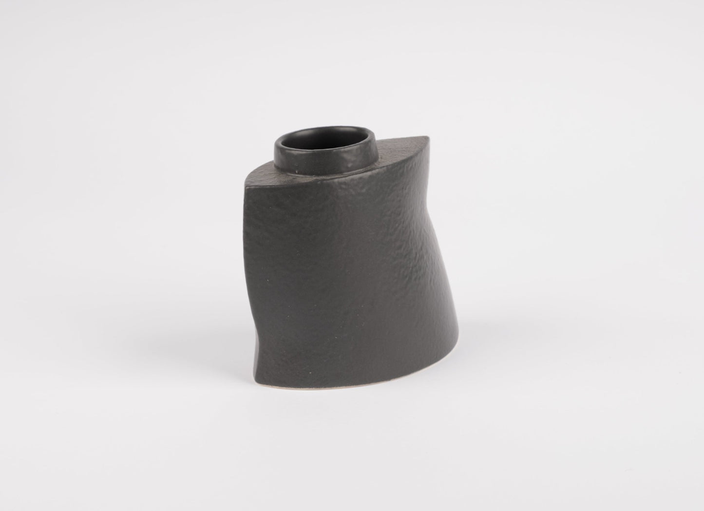 Asymmetrical black stoneware vase with gently faceted matte charcoal finish on white background