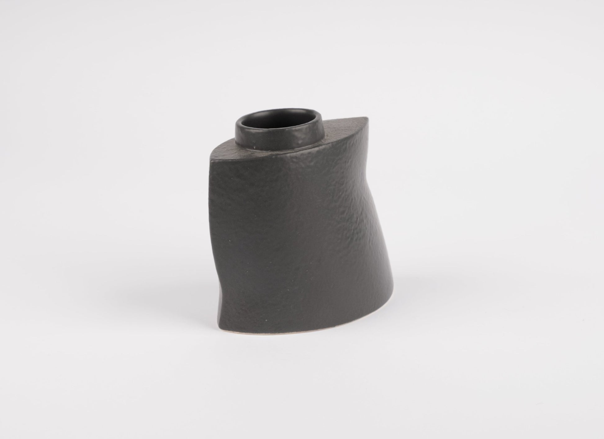 Asymmetrical black stoneware vase with gently faceted matte charcoal finish on white background
