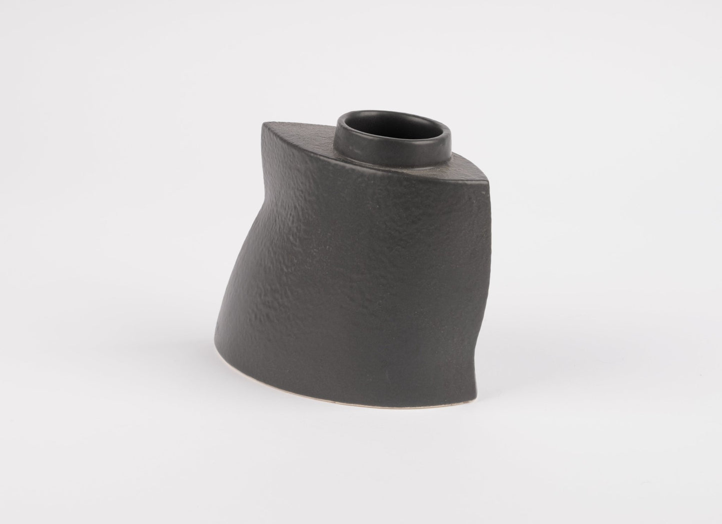Asymmetrical black stoneware vase with gently faceted silhouette and matte charcoal glaze on white background