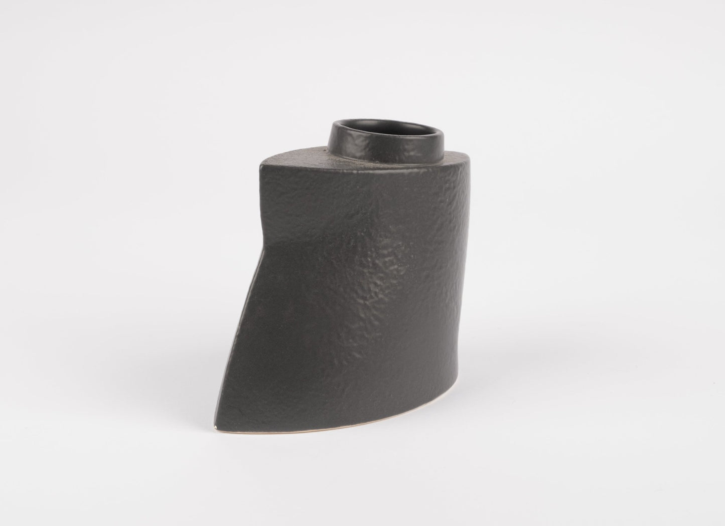 Sculptural black stoneware vase with asymmetrical faceted shape and matte charcoal glaze on white background