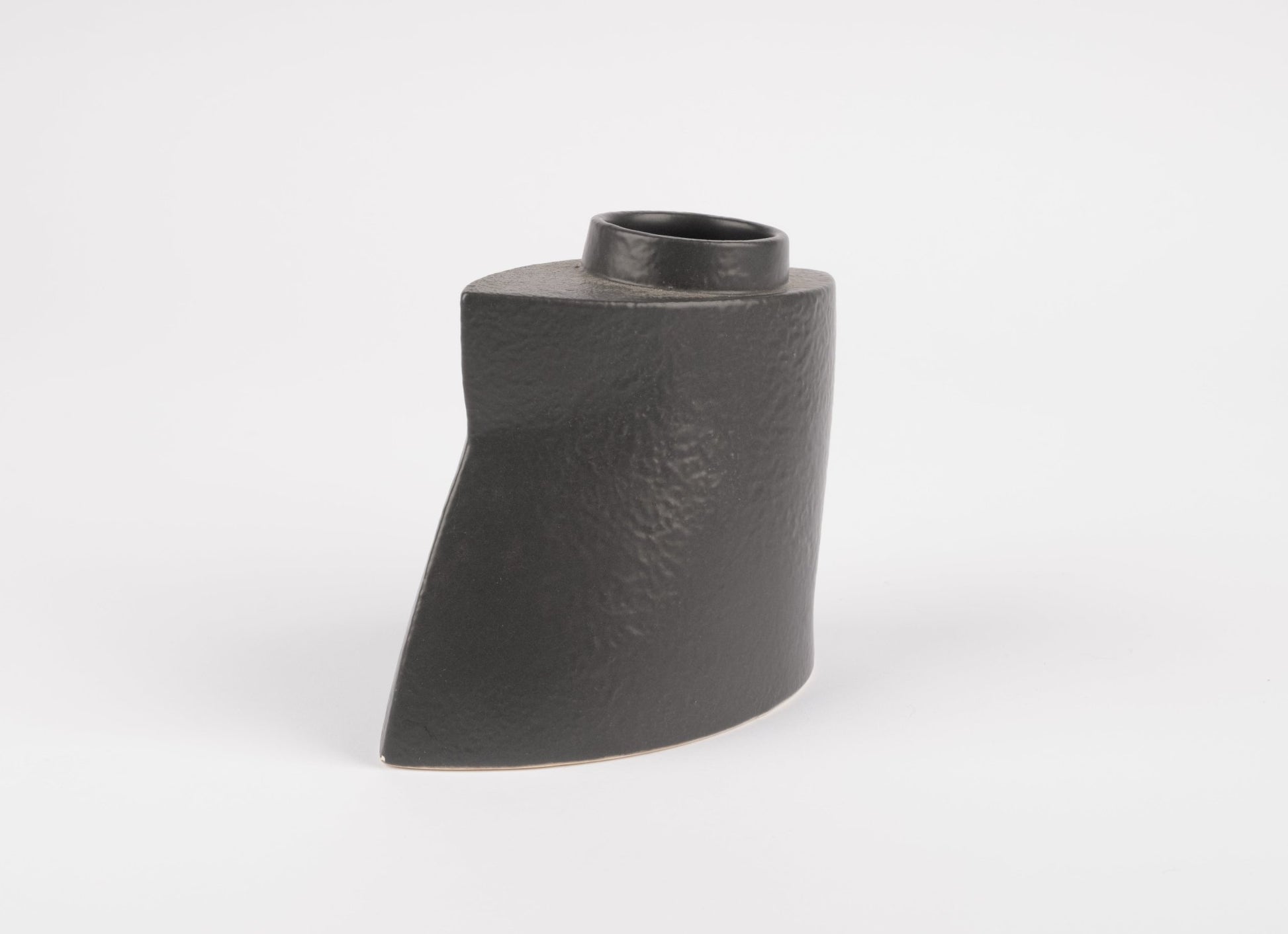 Sculptural black stoneware vase with asymmetrical faceted shape and matte charcoal glaze on white background
