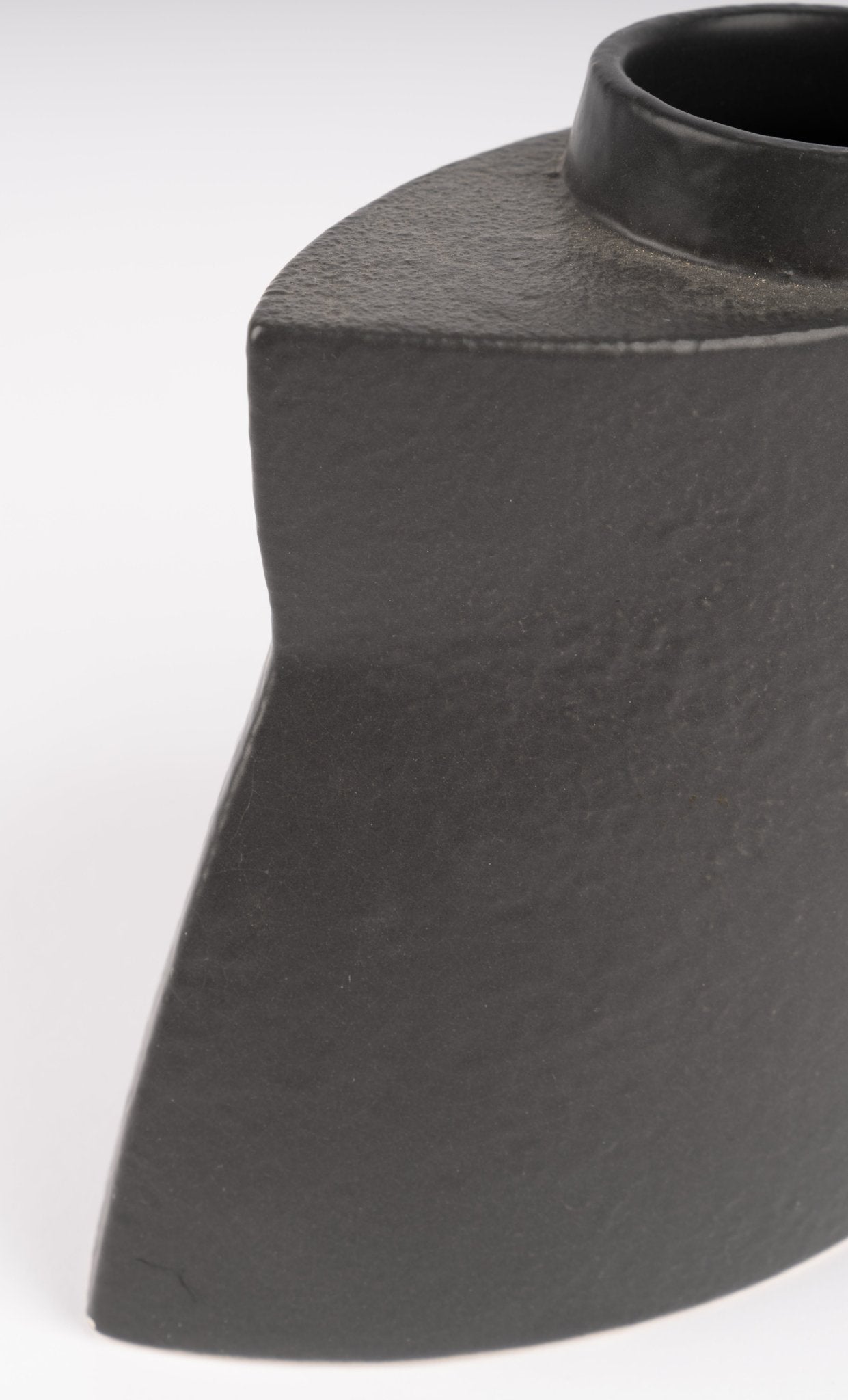 Close-up of sculptural black stoneware vase with asymmetrical faceted silhouette and matte charcoal glaze on white background