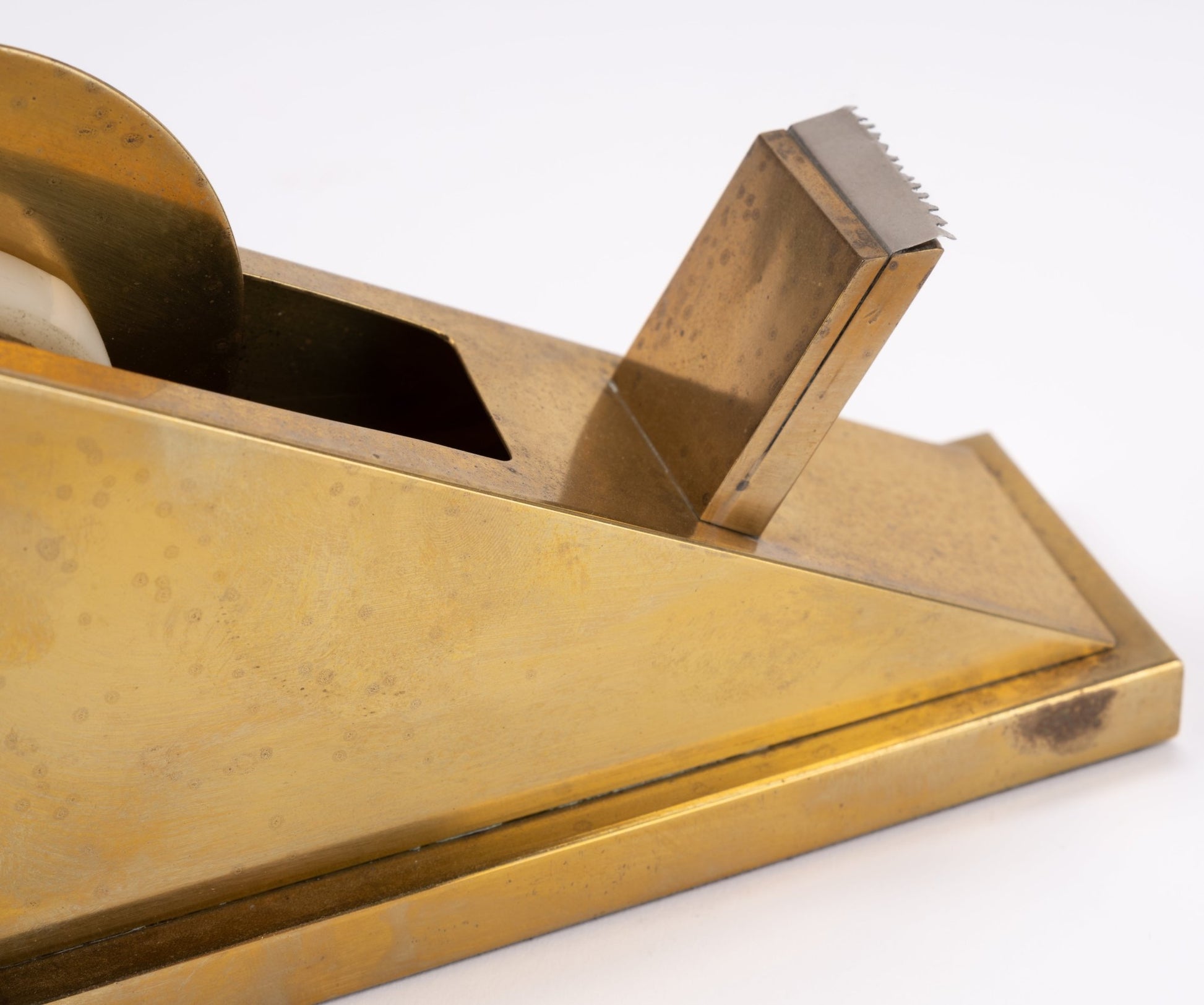 Vintage sculptural brass tape dispenser with minimalist angular form and serrated cutting edge on white background