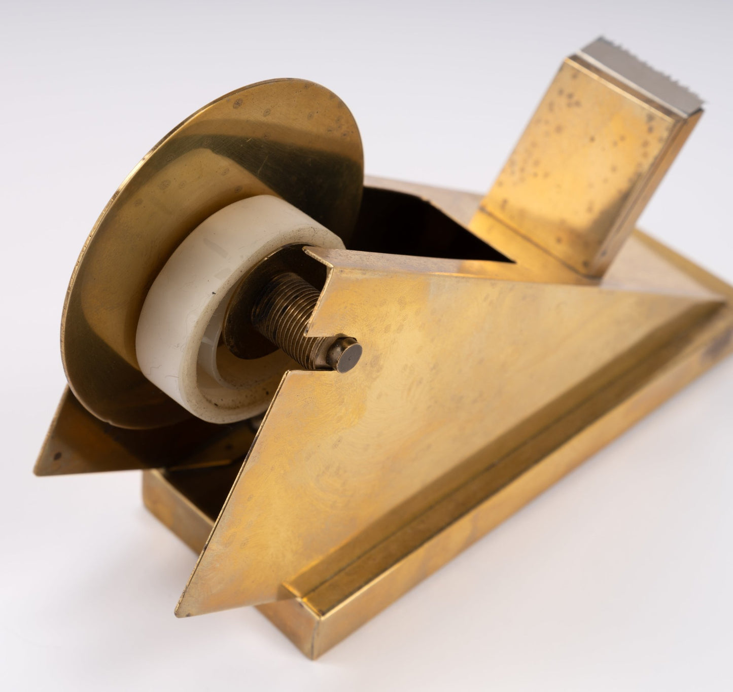 Vintage sculptural brass tape dispenser with angular minimalist design and serrated cutting edge on white background