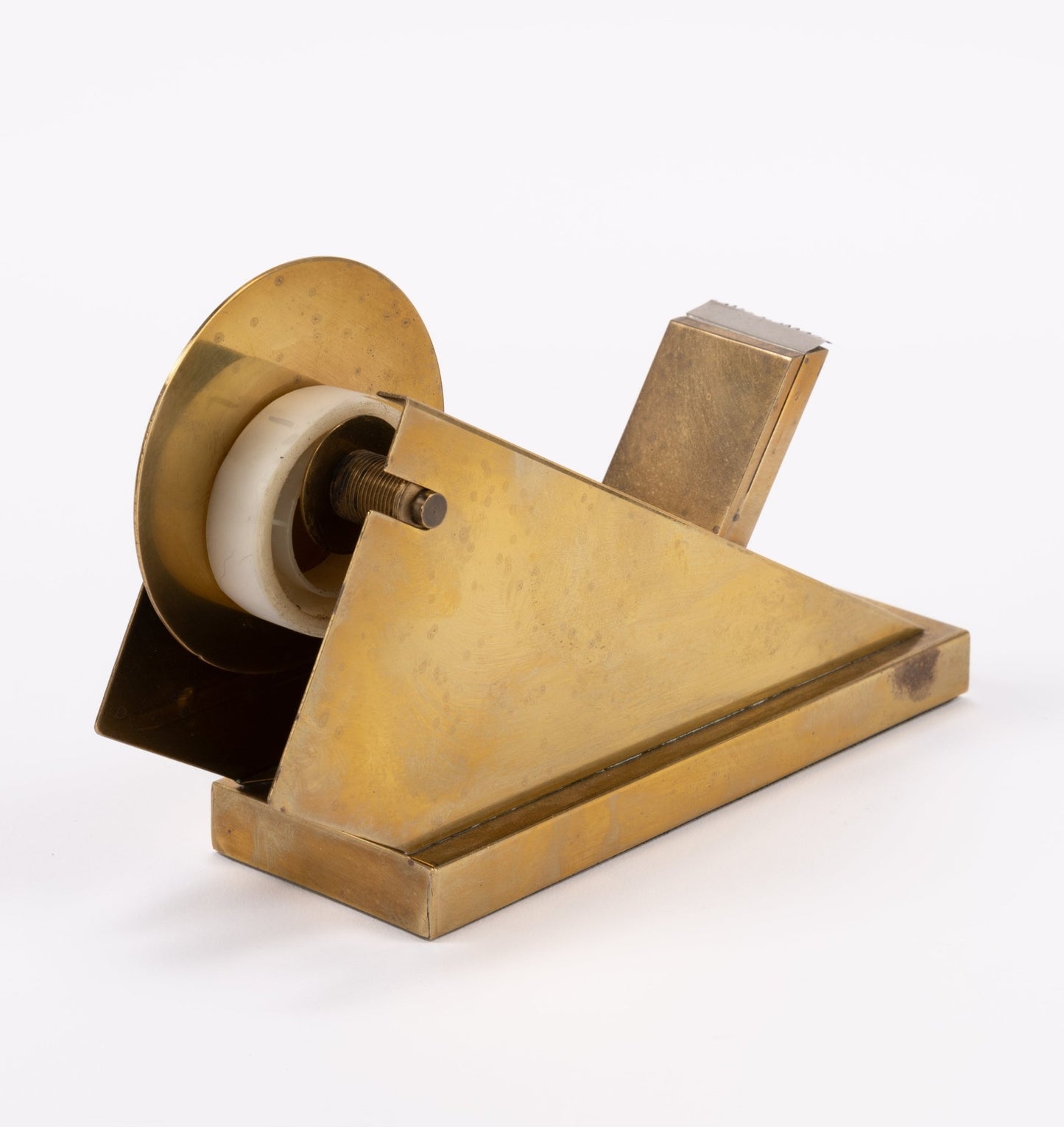 Vintage sculptural brass tape dispenser with geometric minimalist form and built-in serrated cutting edge on white background