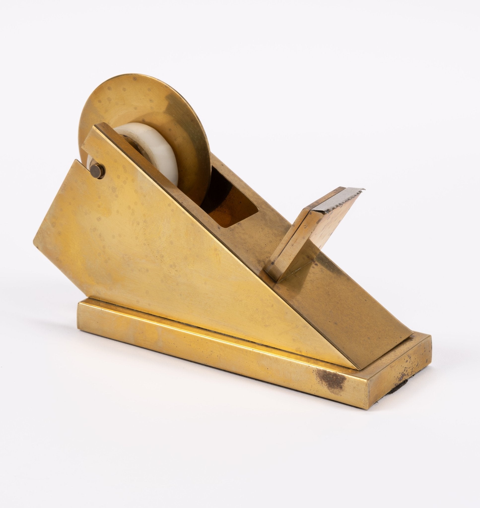 Vintage sculptural brass tape dispenser with minimalist angular form and polished finish on white background