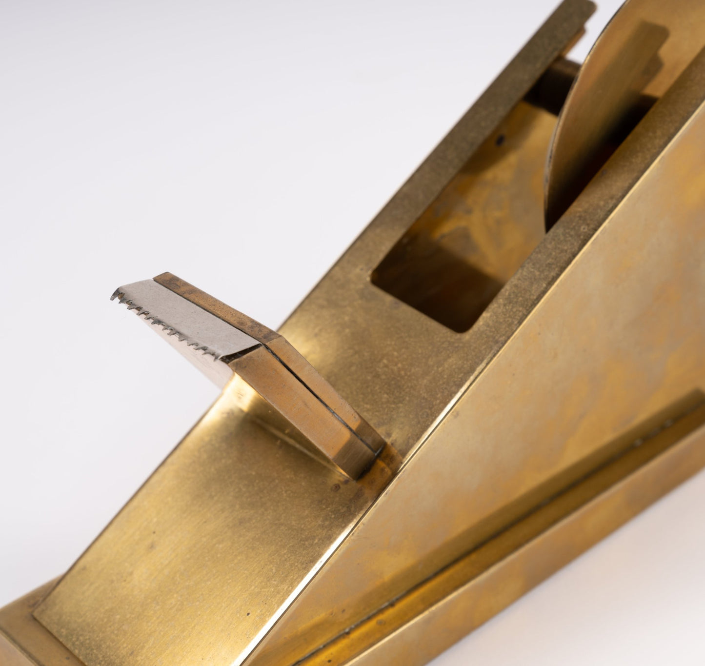 Close-up of sculptural solid brass tape dispenser with minimalist angular design on white background