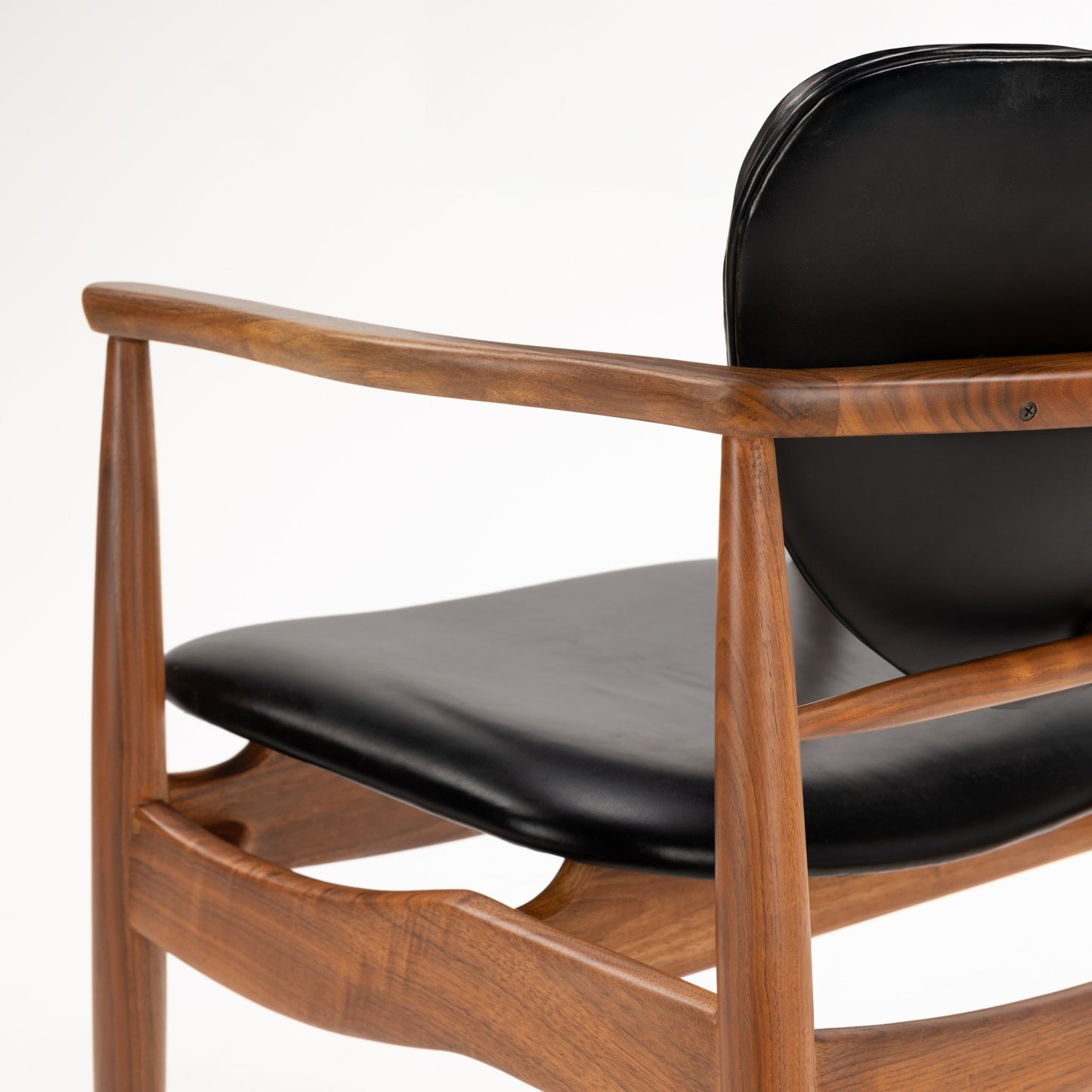 Close-up of smooth walnut armrest and frame paired with black leather seat and backrest of the Set of 4 Walnut Dining Armchairs Attributed to Finn Juhl, reflecting mid century modern furniture design.