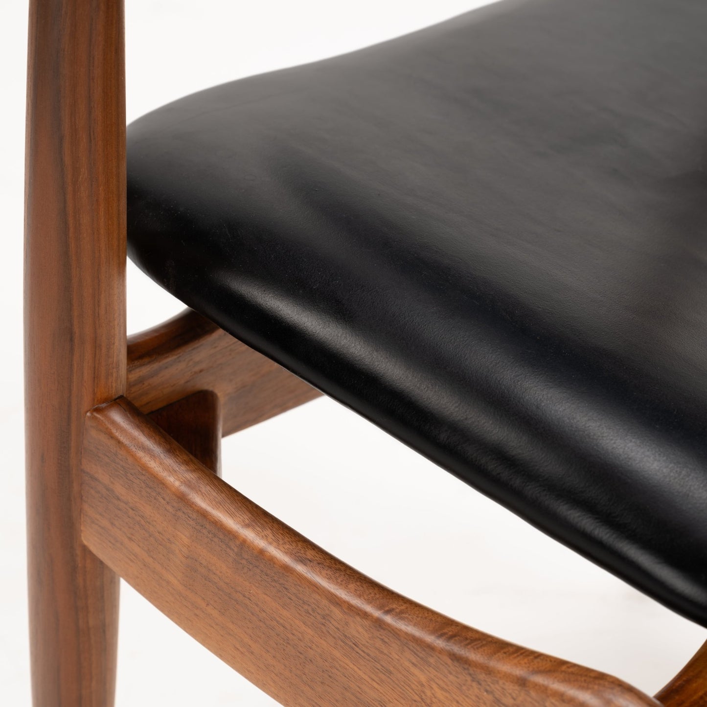 Close-up of the smooth black leather seat cushion and finely crafted walnut frame of the Set of 4 Walnut Dining Armchairs Attributed to Finn Juhl, exemplifying mid century modern seating design.