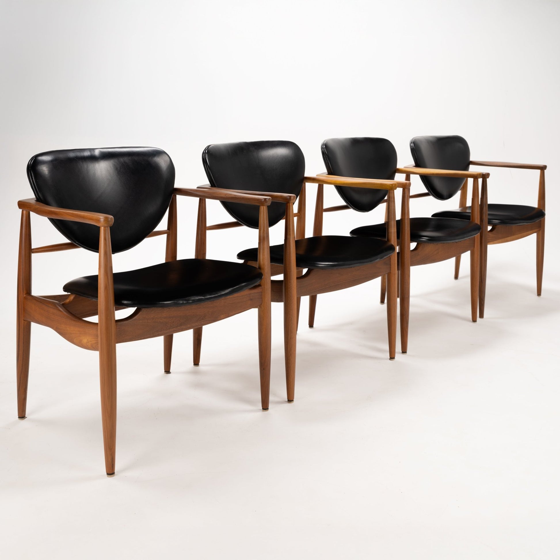 Set of 4 Walnut Dining Armchairs Attributed to Finn Juhl featuring sculpted walnut frames with smooth black leather seats and curved backrests, embodying vintage Danish mid century modern seating design.