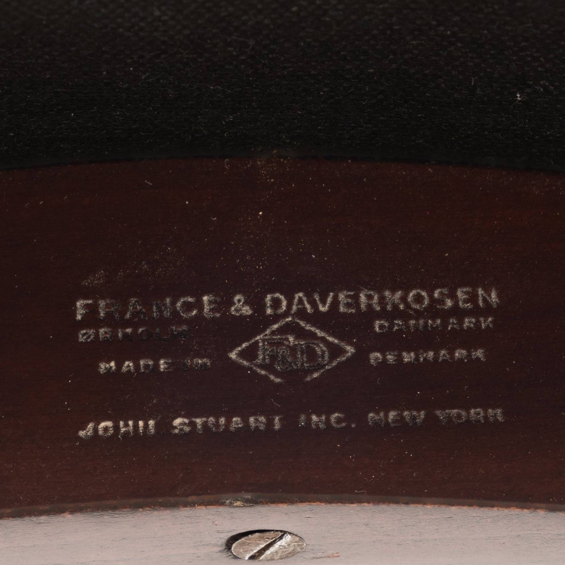 Close-up of a wooden frame label on the Sigvard Bernadotte Model FD132 Sofa, indicating craftsmanship by France & Daverkosen in Denmark and distribution by John Stuart Inc., New York.