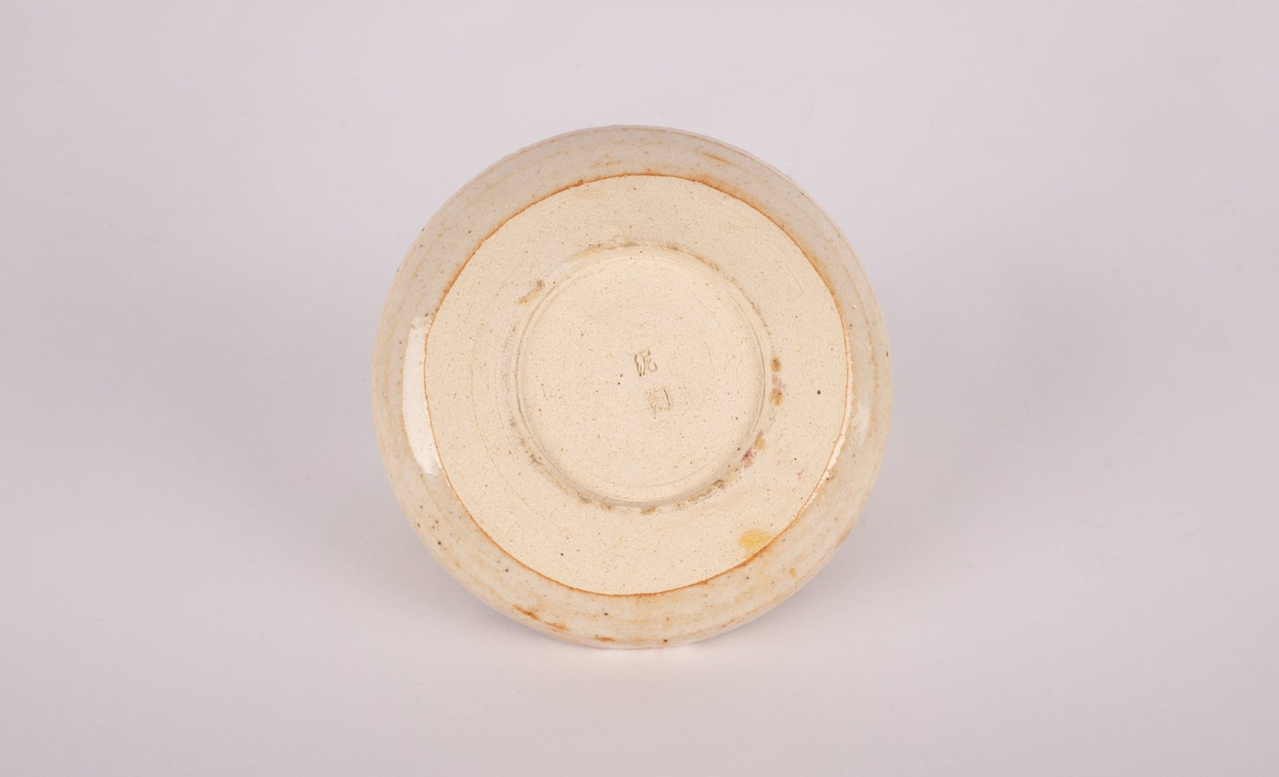 Bottom view of small studio pottery bowl with stamped signature and natural glaze finish on neutral background