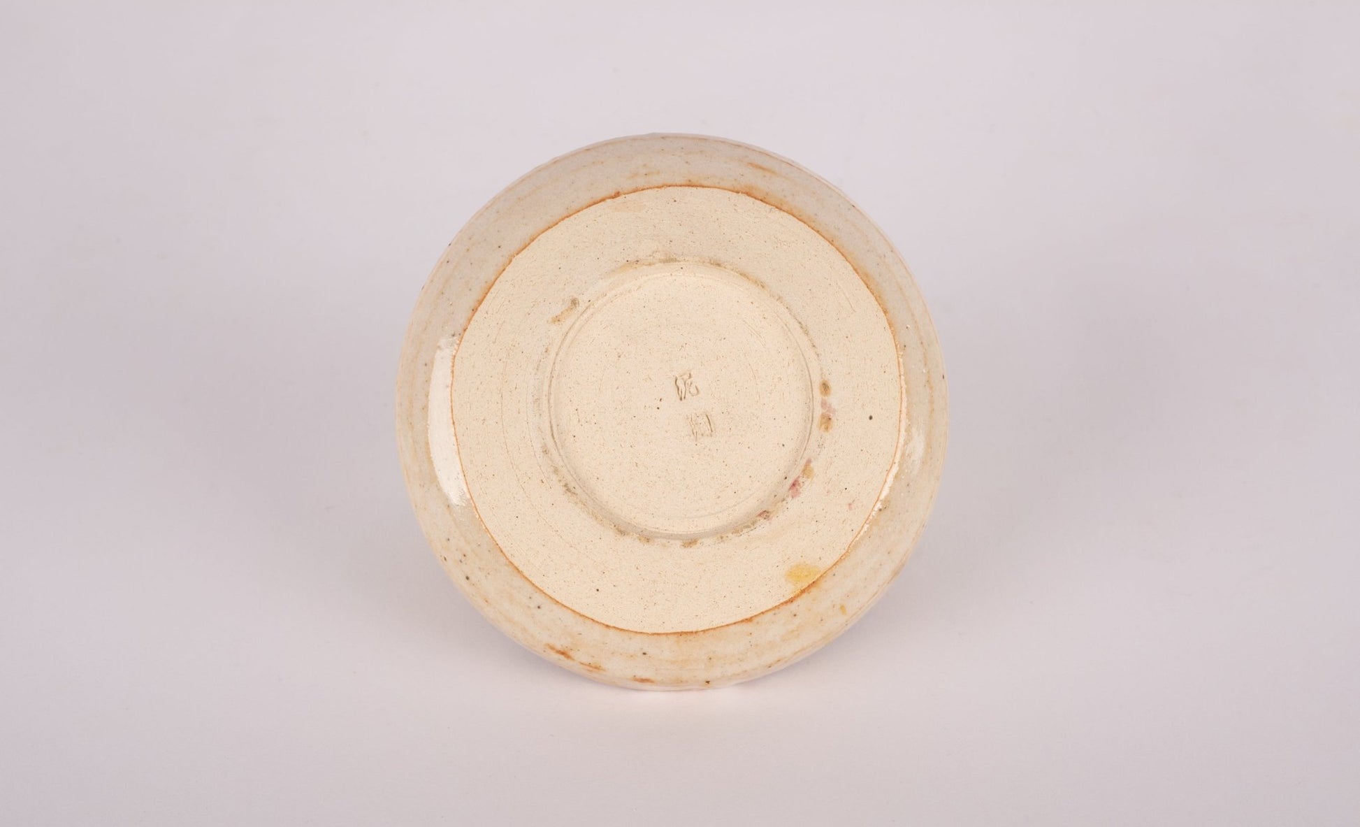 Bottom view of small studio pottery bowl with stamped signature and natural glaze finish on neutral background
