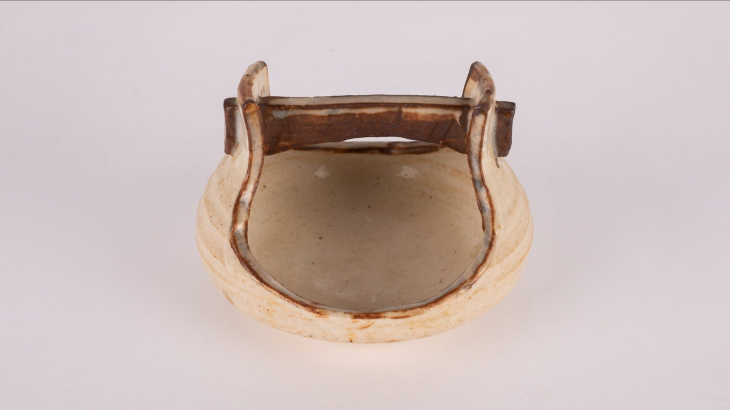 Small studio pottery bowl with handle and natural glaze, featuring stamped signature on the bottom.