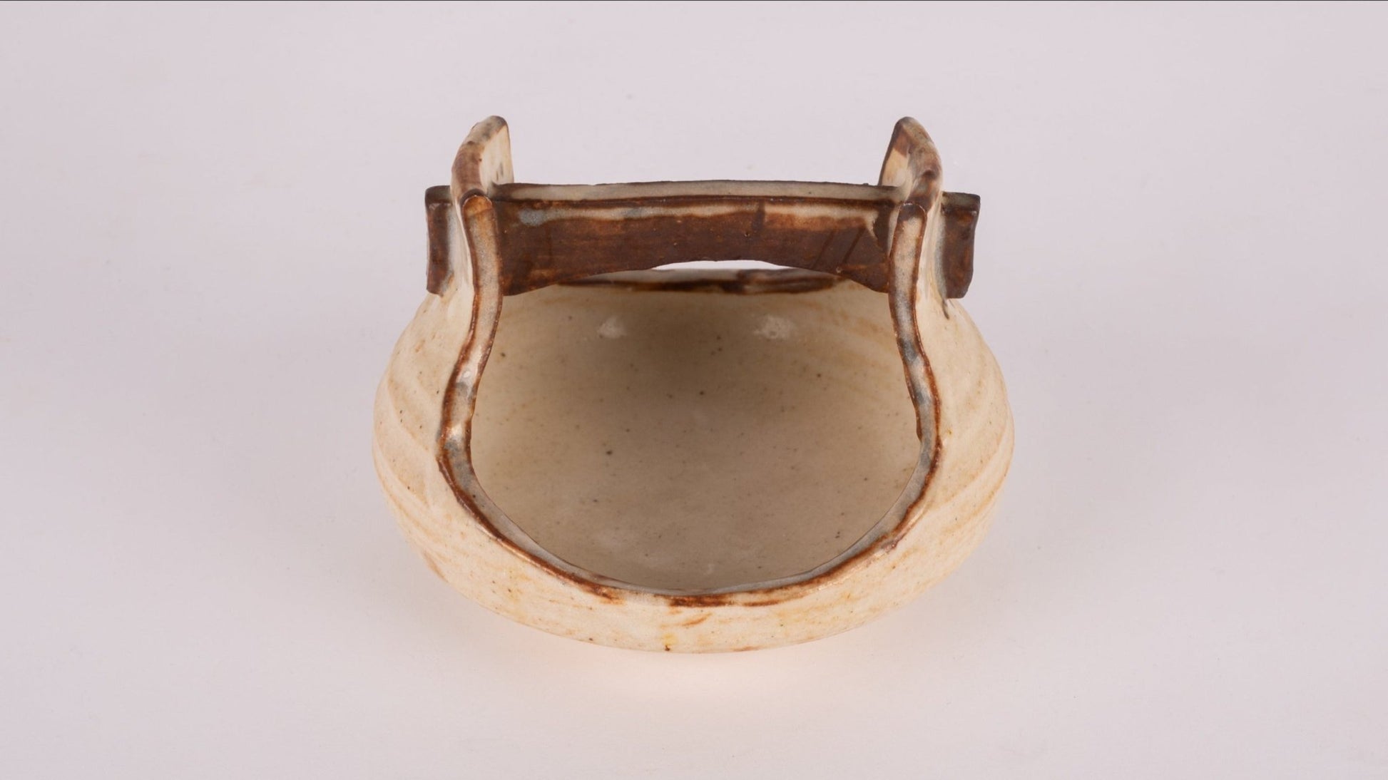 Small studio pottery bowl with handle and natural glaze, featuring stamped signature on the bottom.