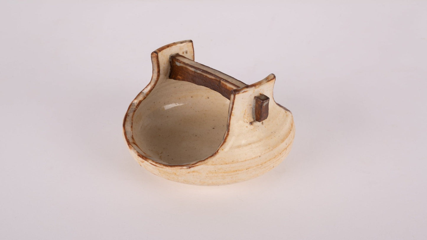 Small studio pottery bowl with handle and stamped signature on bottom, in natural beige glaze finish.